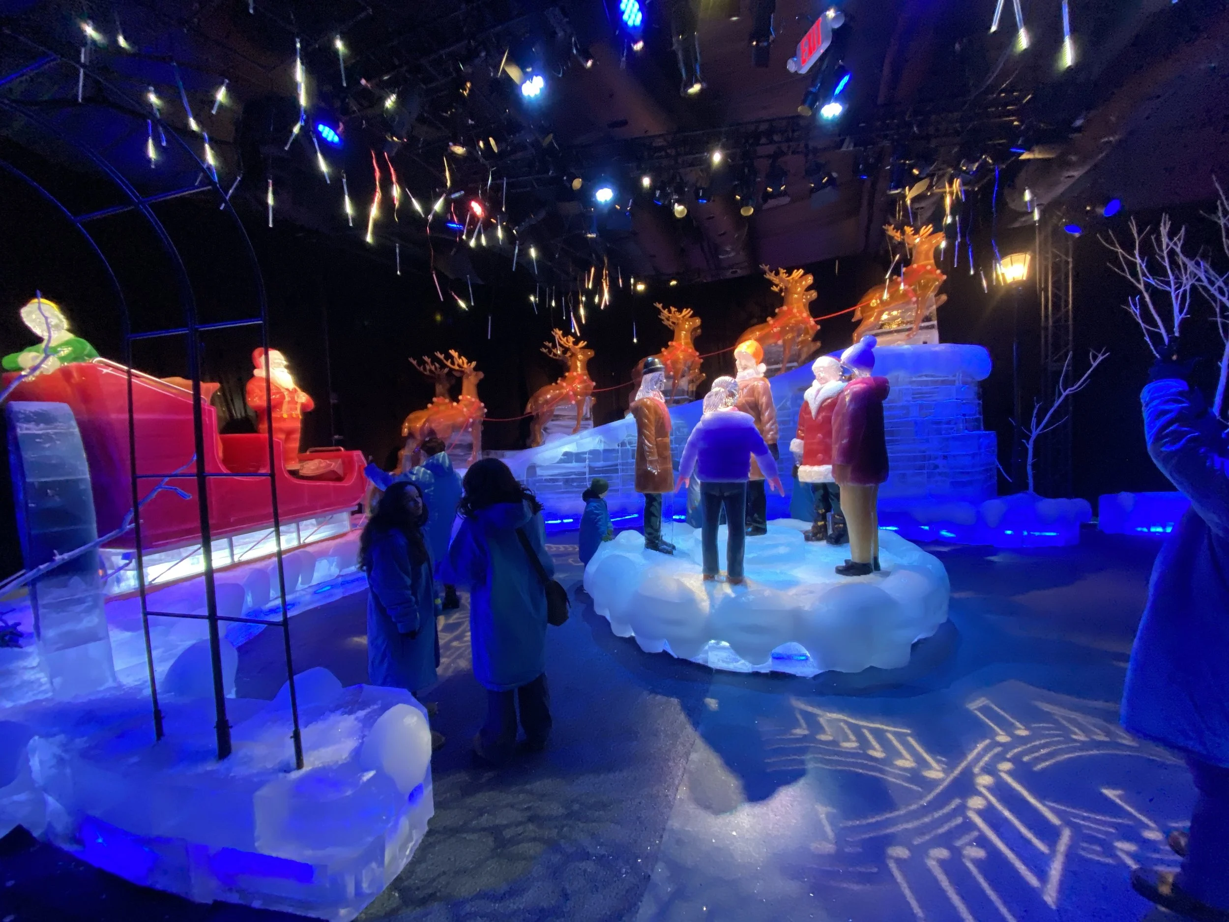 Indoor ice skating rink holiday display with inflatable Santa Claus, reindeer, snowmen, figures skating, and holiday lights.