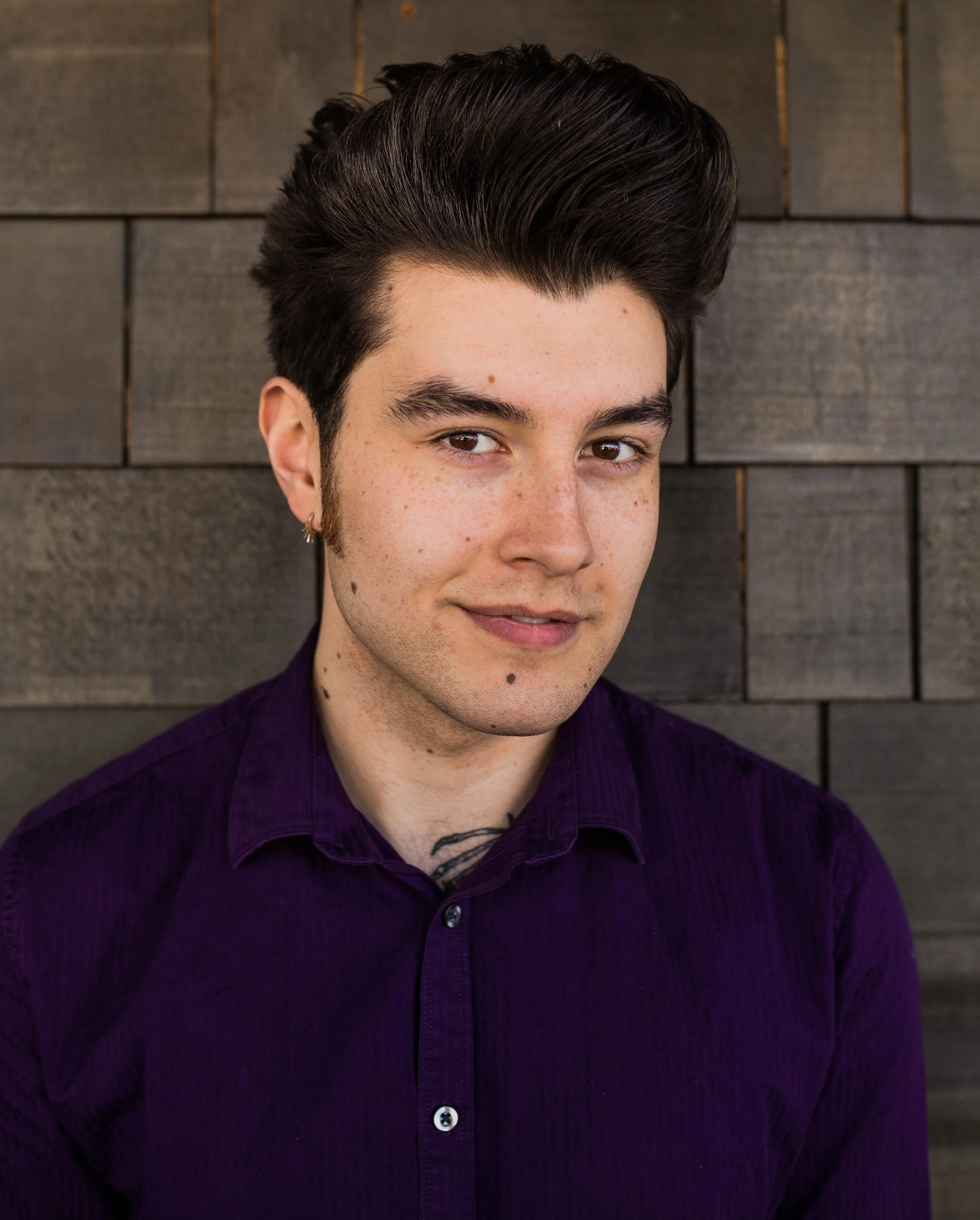 A young man with dark, styled hair, fair skin with freckles, wearing a purple shirt, standing in front of a wooden wall. Seattle professional head shot photography