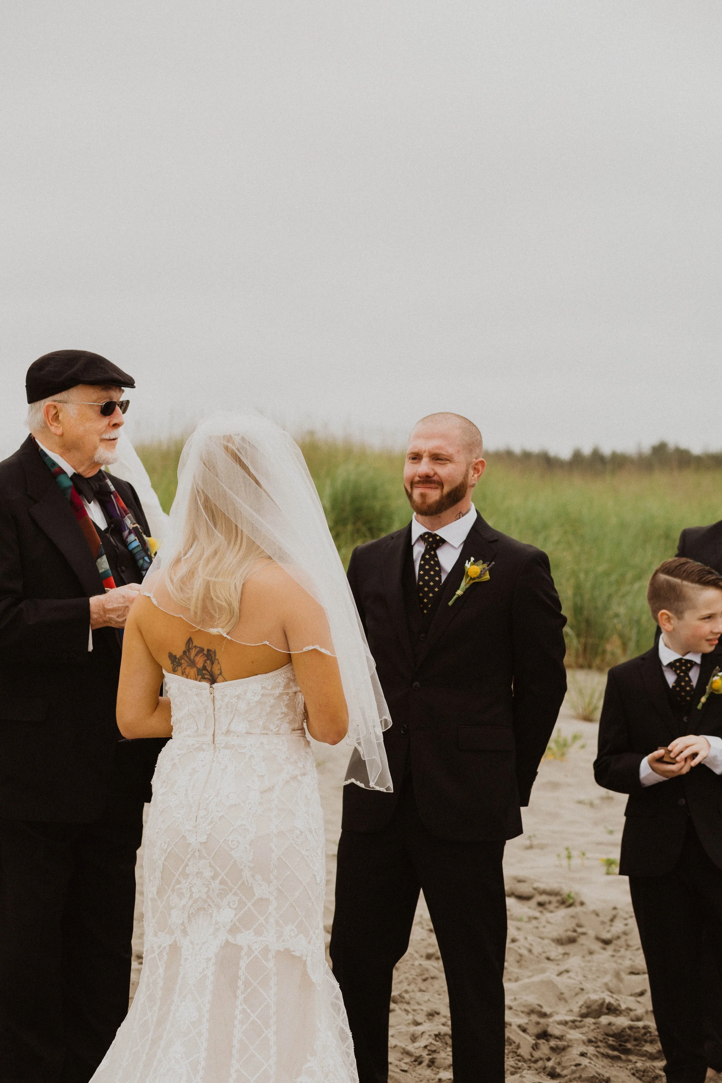 A wedding ceremony taking place on a beach with a bride, groom, officiant, and two young boys dressed in black suits. Long Beach, WA wedding photography.