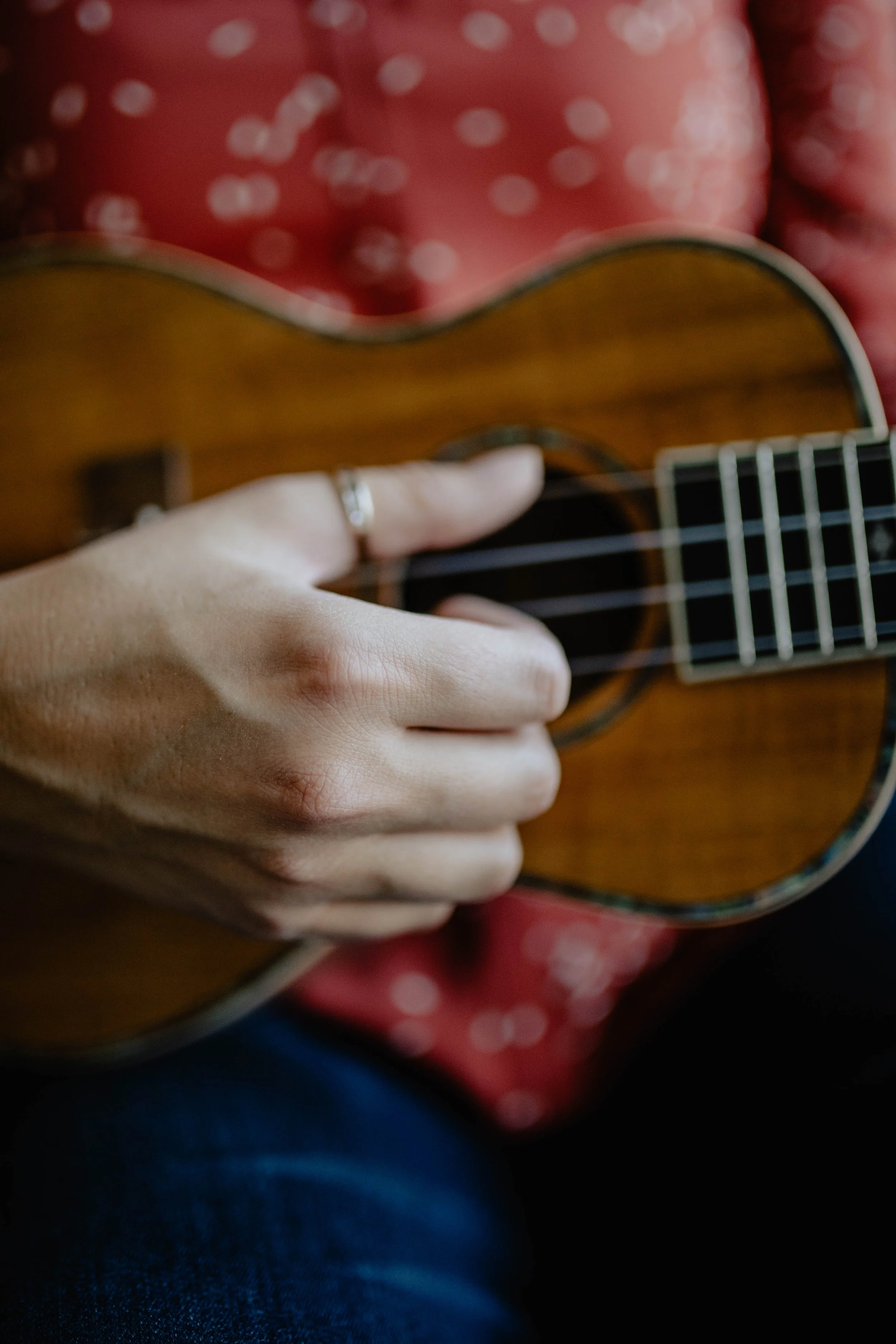 Close-up of a person playing a small wooden acoustic guitar, wearing a red polka-dotted shirt. Seattle professional head shot photography