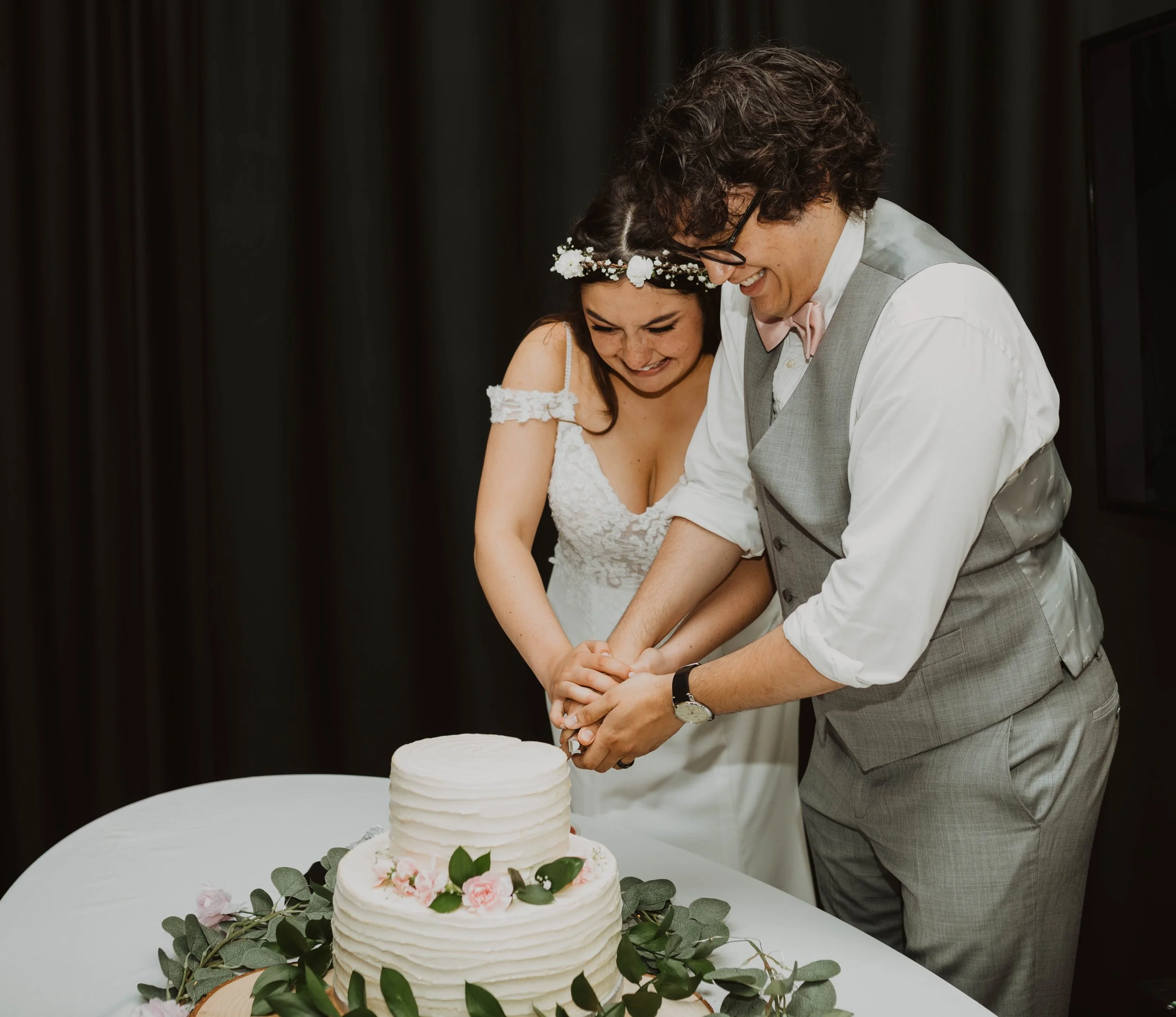 A couple cutting a wedding cake together at their wedding reception, smiling and happy. Seattle, WA wedding photography.