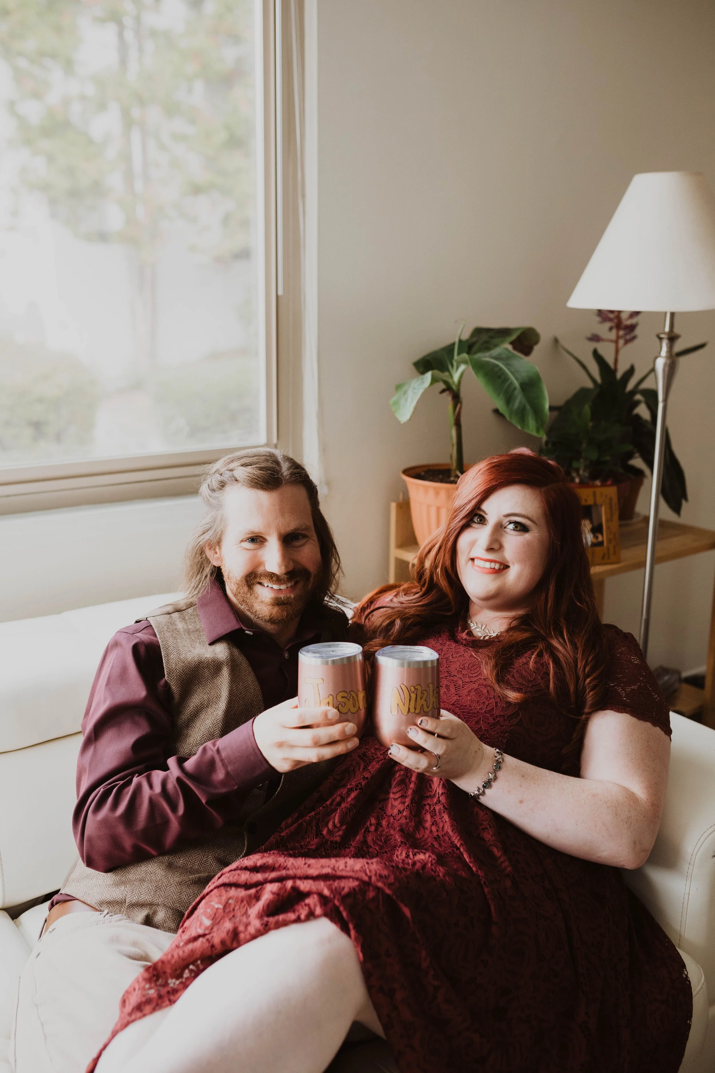 A couple celebrating with personalized cans while sitting on a white couch in a cozy living room with plants and a lamp. Pioneer Square, Seattle, WA wedding photography.