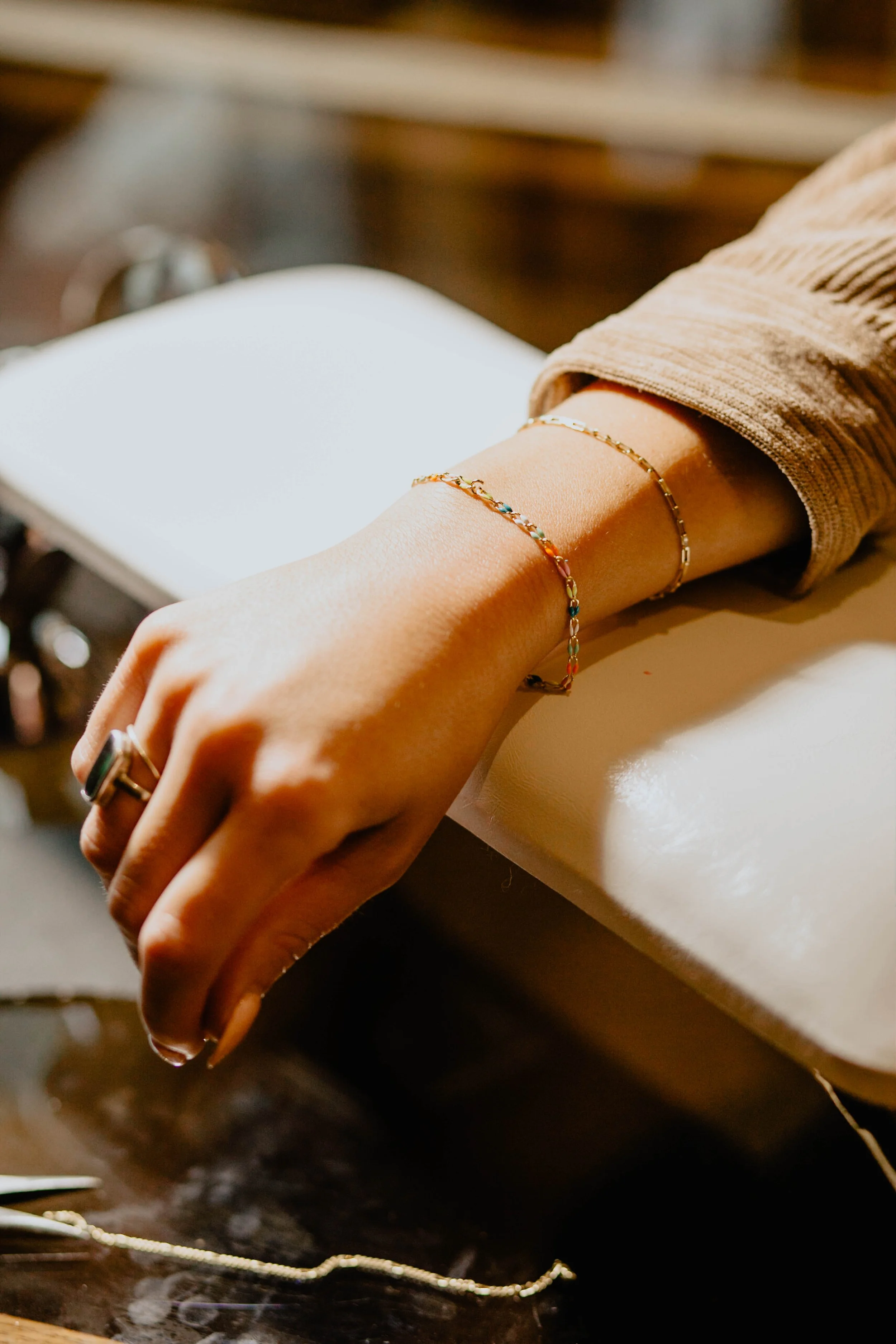 A person's hand resting on a white surface, wearing colorful and gold jewelry, with a blurred background. Seattle professional head shot photography