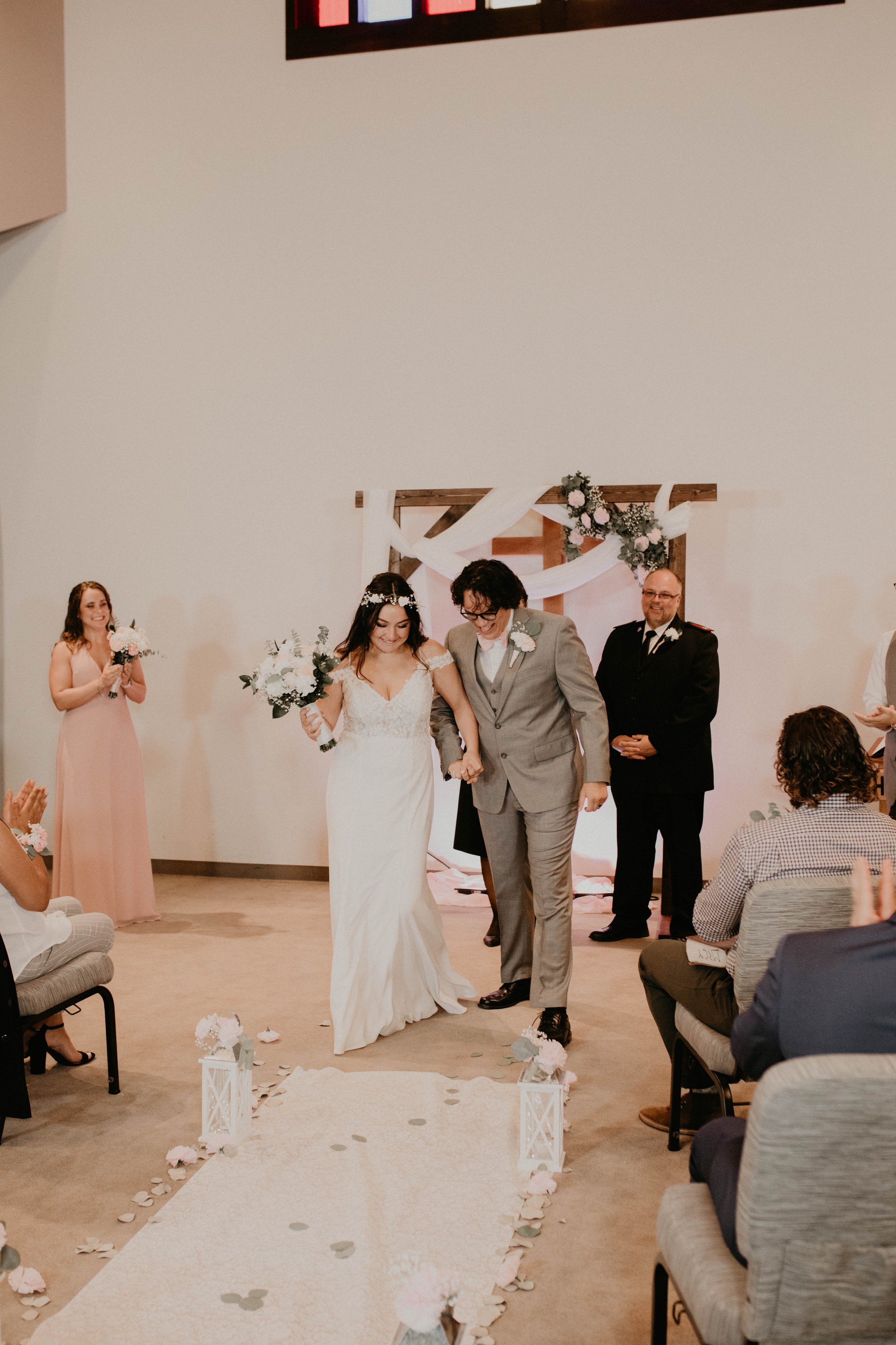 A bride and groom walking hand in hand down the aisle during their wedding ceremony, surrounded by guests and floral decorations. Seattle, WA wedding photography.
