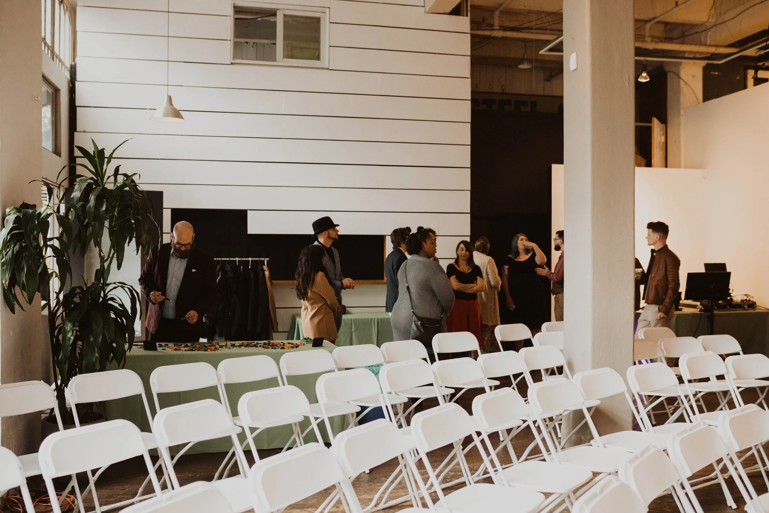 People socializing at a gathering in a modern, minimalistic room with white chairs and large potted plant. Pioneer Square, Seattle, WA wedding photography.