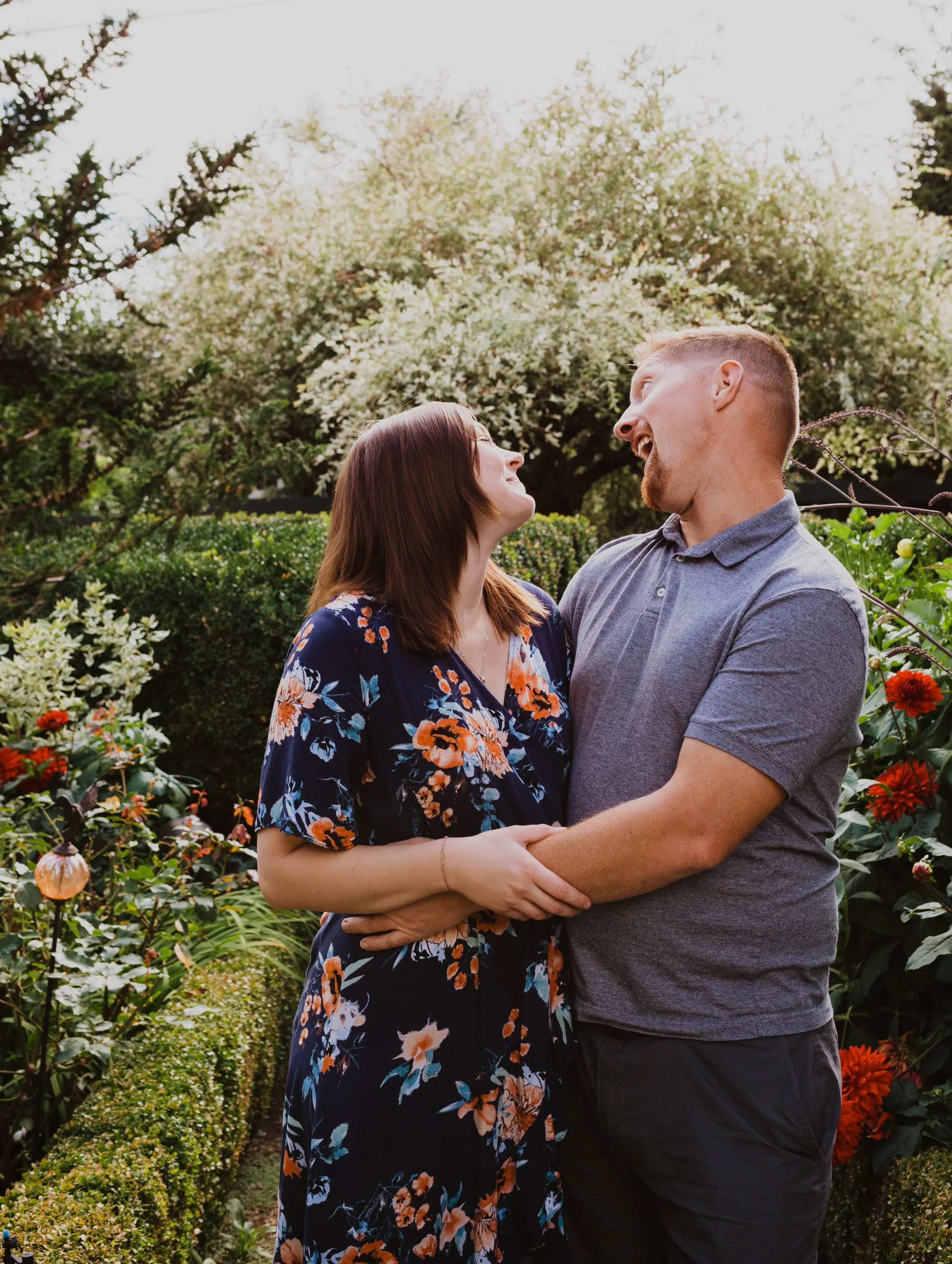 A couple smiling and looking at each other in a garden with blooming flowers and greenery. Seattle, WA wedding photography.