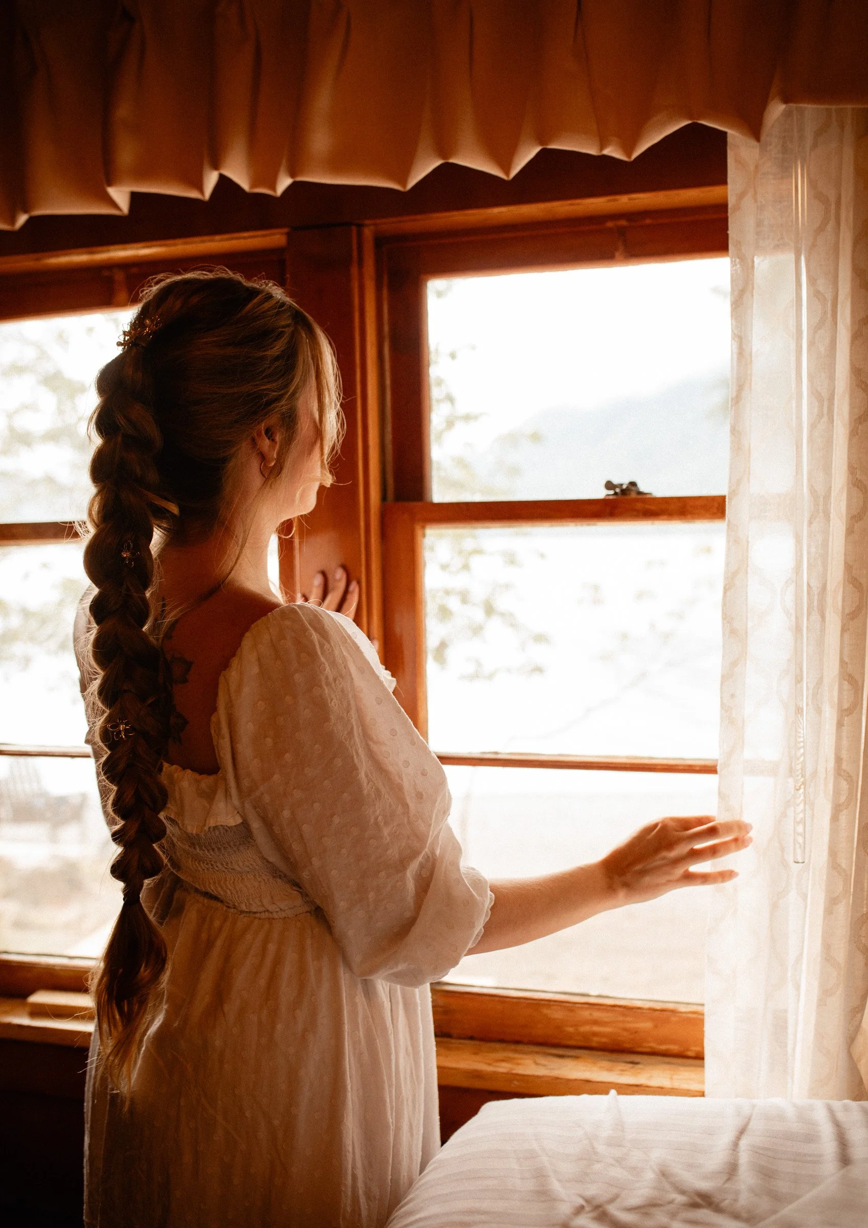 Bride gazing out the window in a quiet, romantic moment before getting dressed for her Lake Crescent wedding at Lake Crescent Lodge in Port Angeles, Washington.