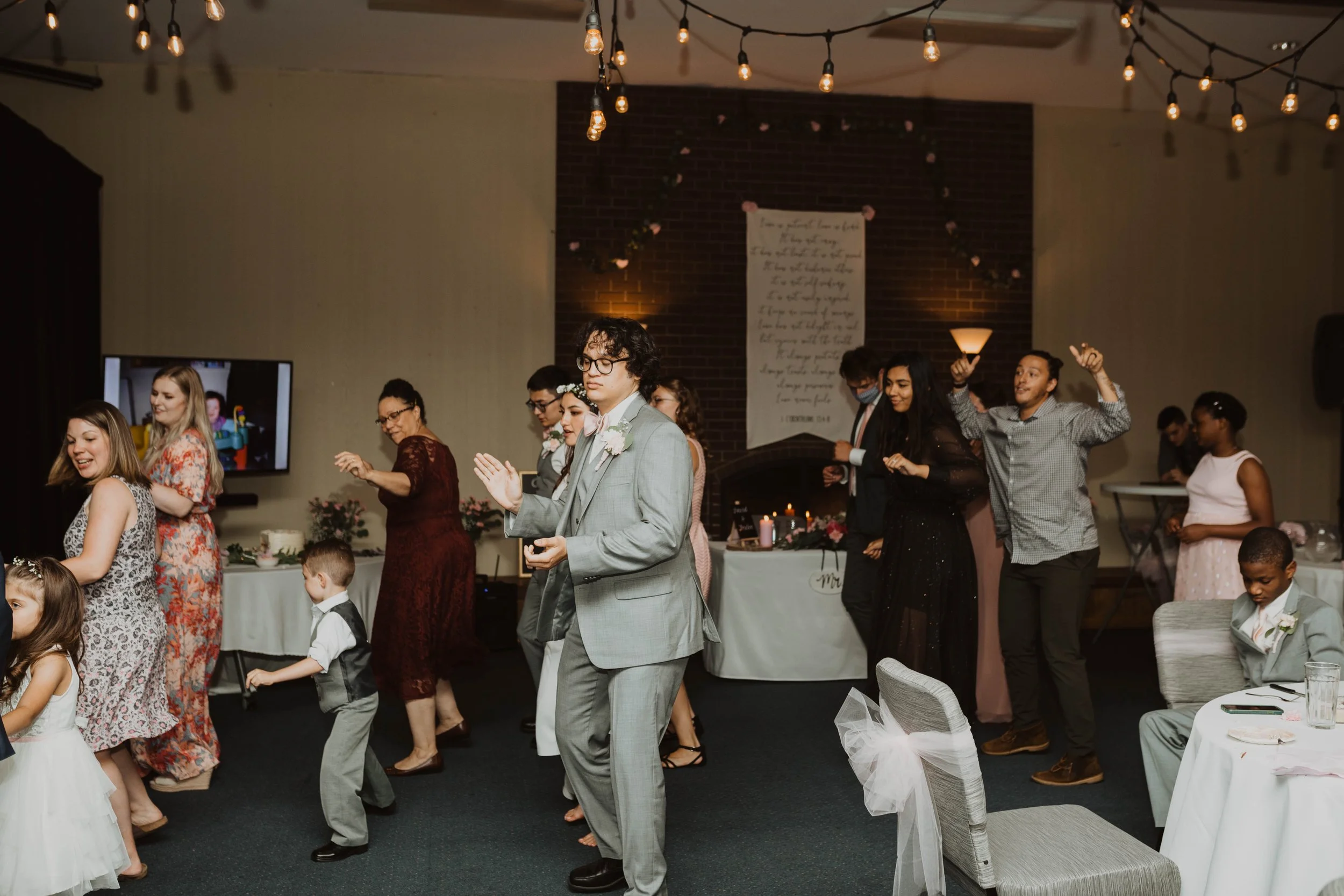 People dancing at wedding reception in a decorated indoor venue with string lights and a brick wall in the background. Seattle, WA wedding photography.