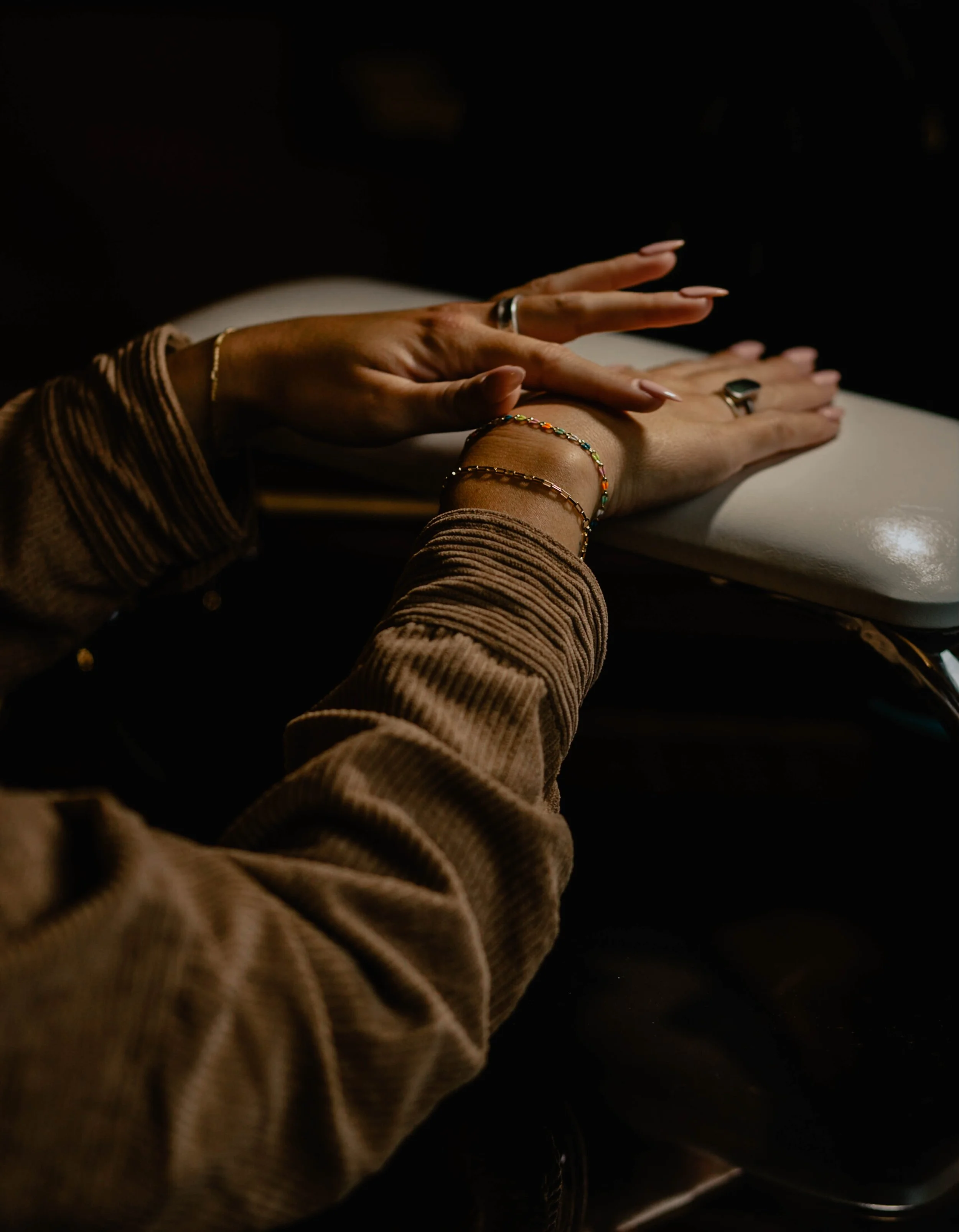 Person placing their hand on a nail technician's hand during a manicure, with jewelry on their fingers and wrist, in a dimly lit setting. Seattle professional head shot photography