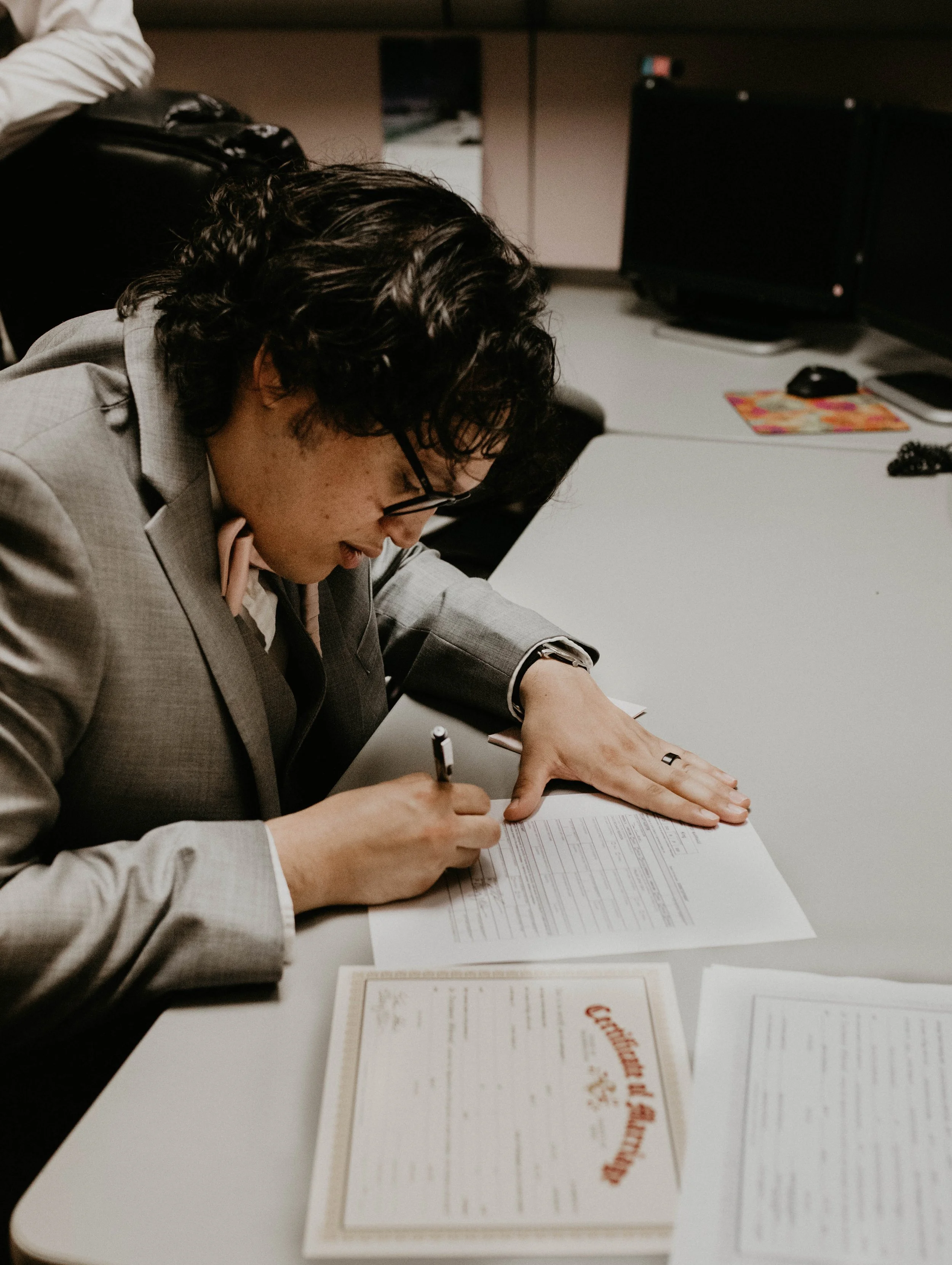 Person in a gray suit signing a document at a desk in an office. Seattle, WA wedding photography.