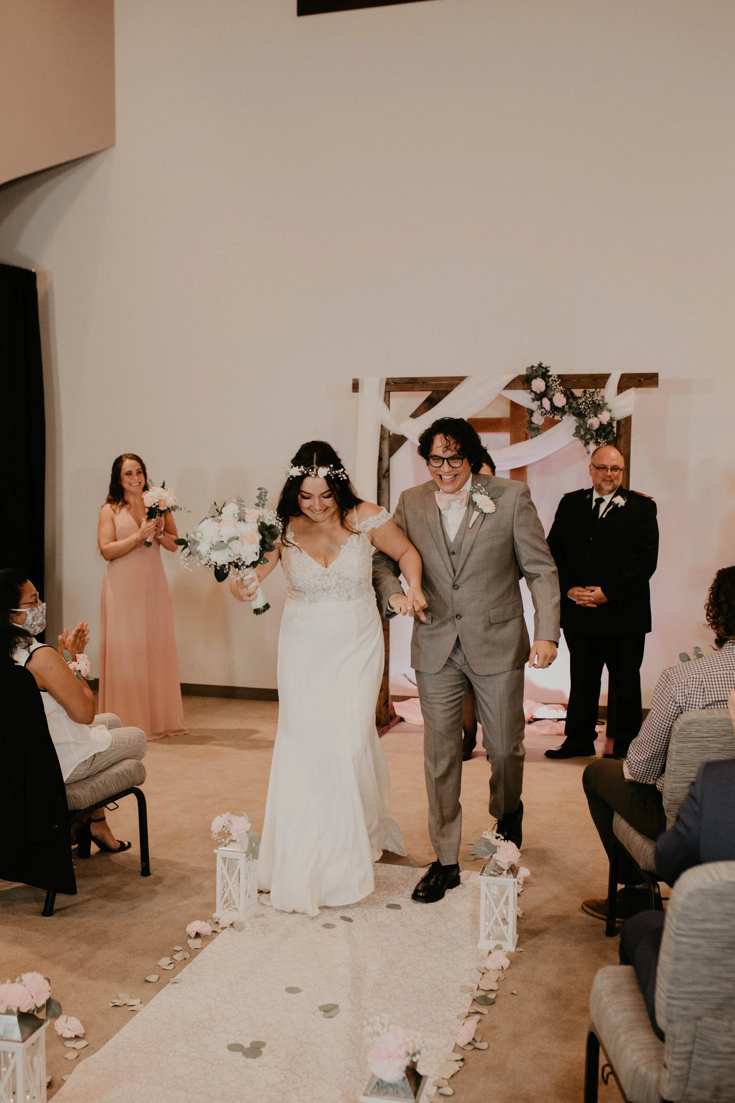 A newlywed couple walking down the aisle at their wedding ceremony, smiling and holding hands, with guests and bridesmaids in the background. Seattle, WA wedding photography.