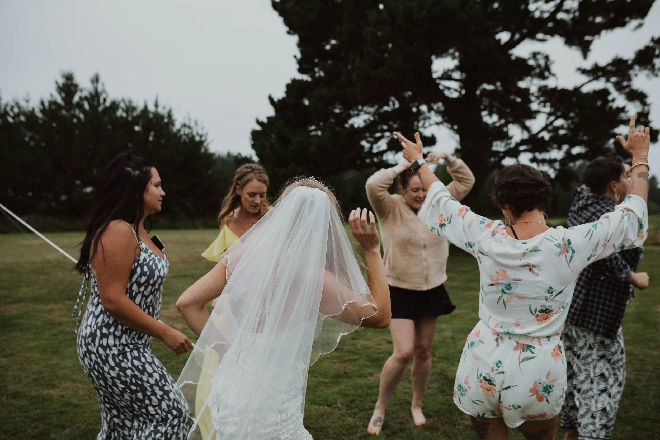 Group of women dancing outdoors during a wedding celebration, with a bride wearing a veil in the center. Long Beach, WA wedding photography.