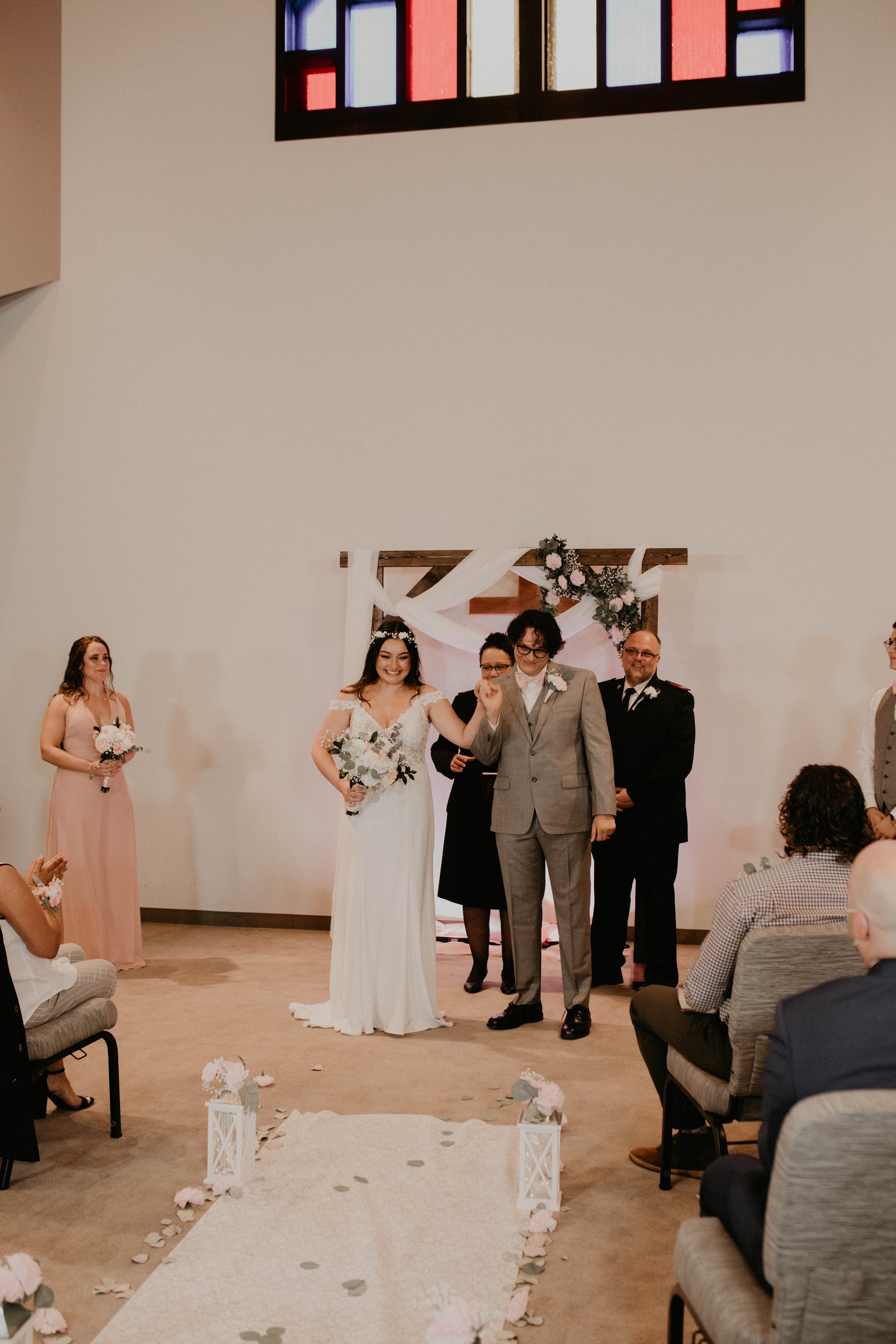 Wedding ceremony with a bride and groom holding hands, standing with officiant and wedding party in a church with stained glass window Seattle, WA wedding photography.