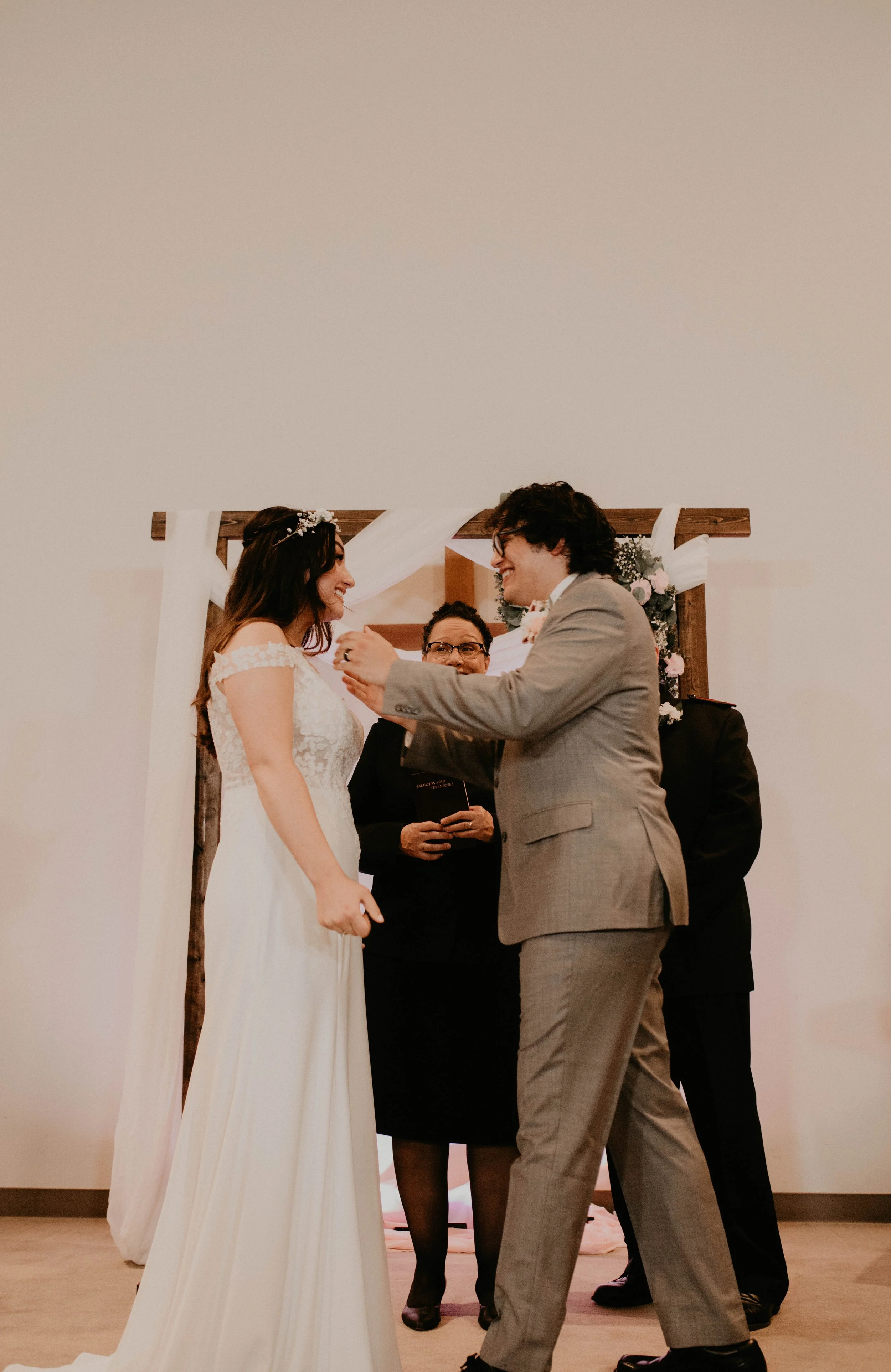 A bride and groom exchange vows during a wedding ceremony in front of an officiant, with floral decorations and a wooden arch in the background. Seattle, WA wedding photography.