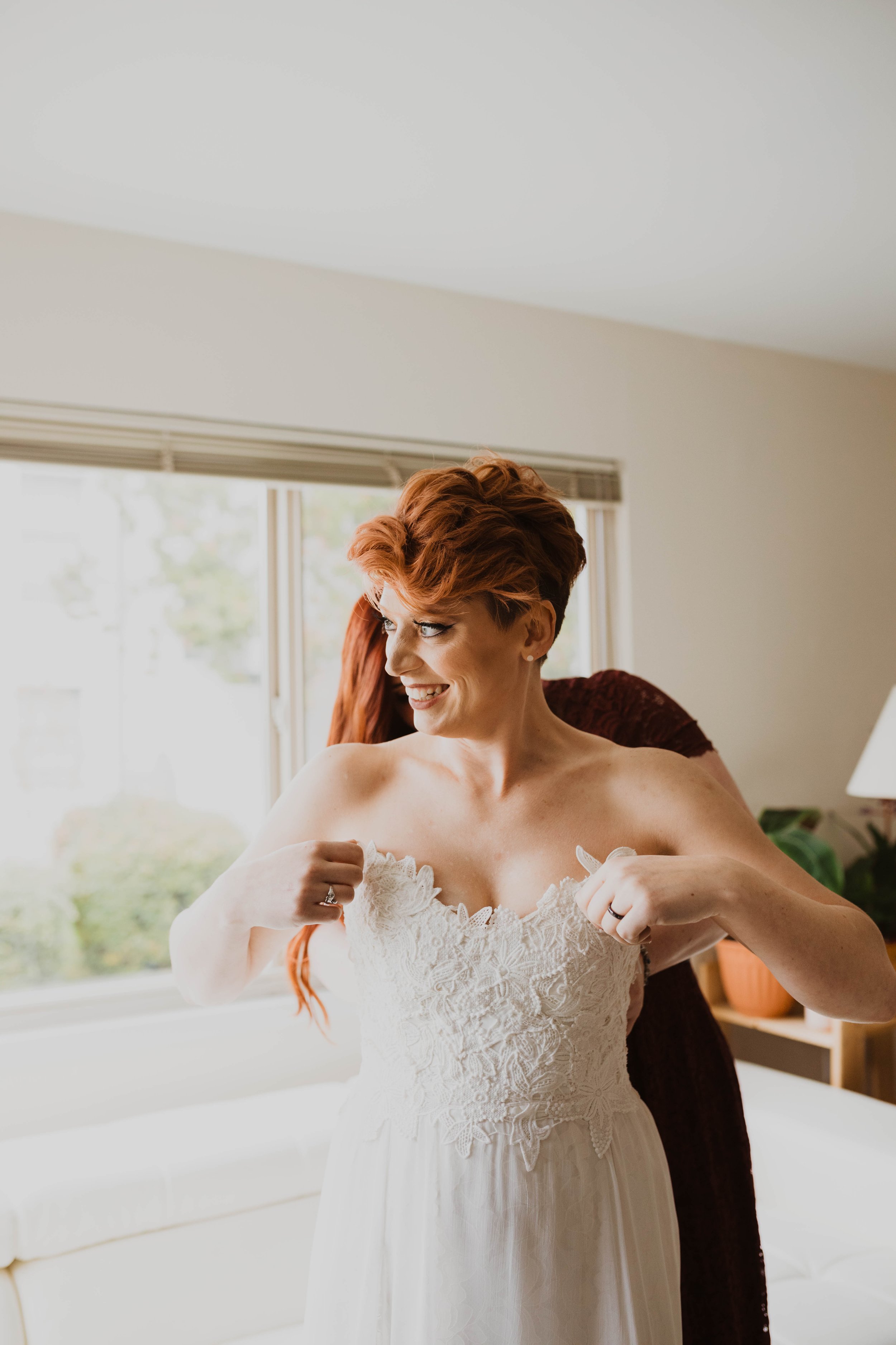 A woman in a wedding dress smiling while someone helps her get dressed. Pioneer Square, Seattle, WA wedding photography.