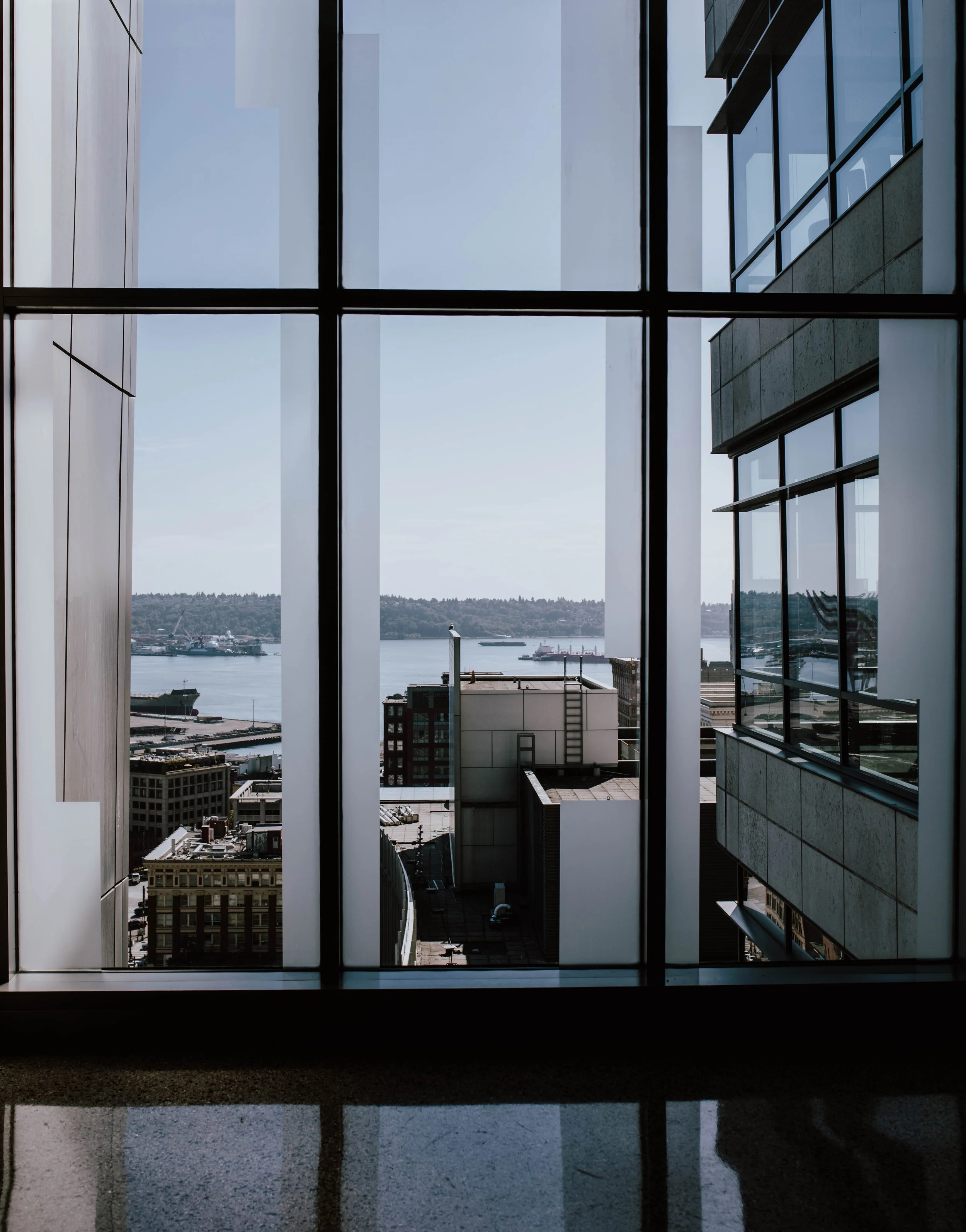 View through a large window showing a cityscape with buildings and water, framed by the window's grid. Seattle Municipal Courthouse wedding photography.