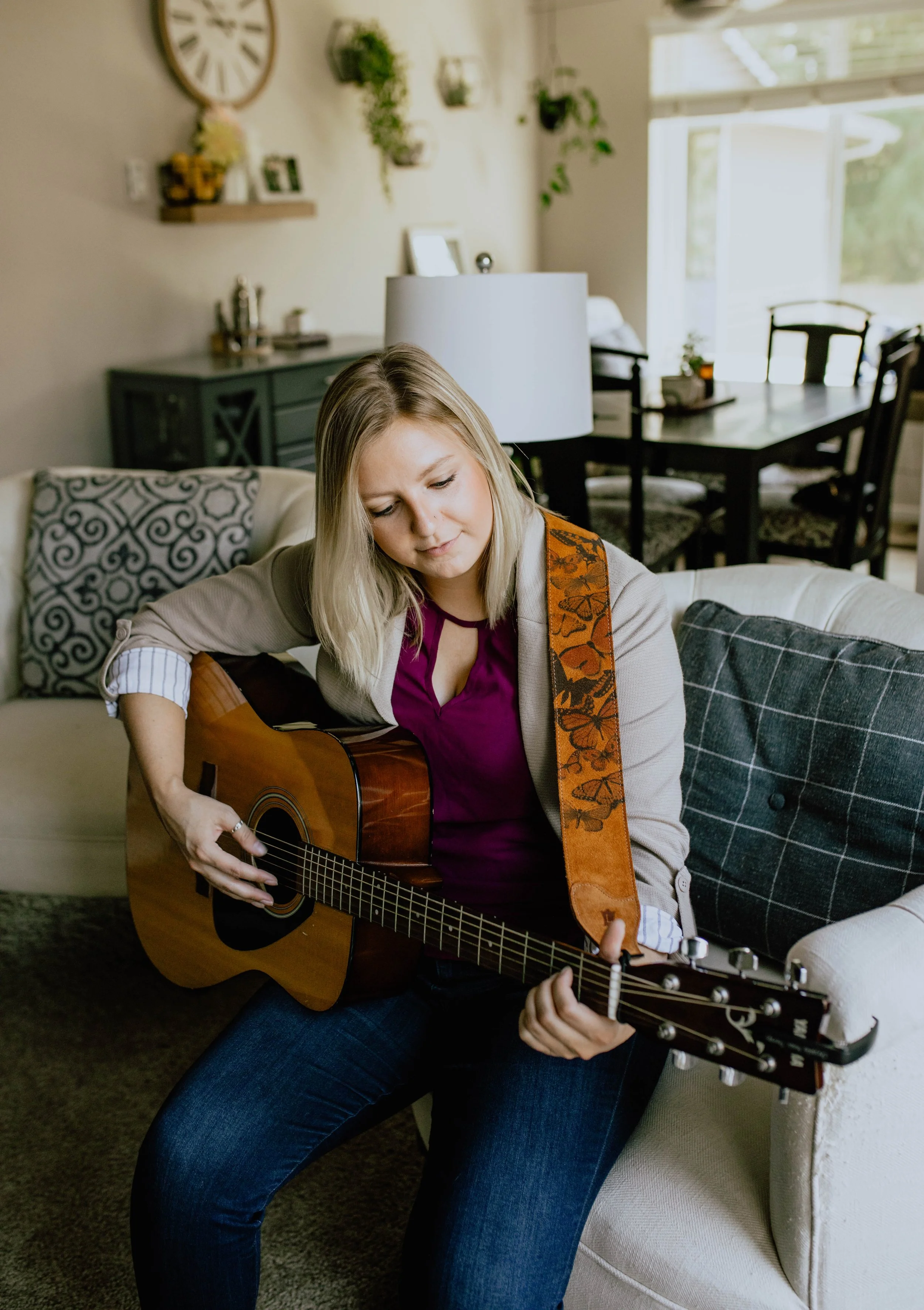 A woman sitting on a cream-colored sofa playing an acoustic guitar in a cozy living room. Seattle professional head shot photography