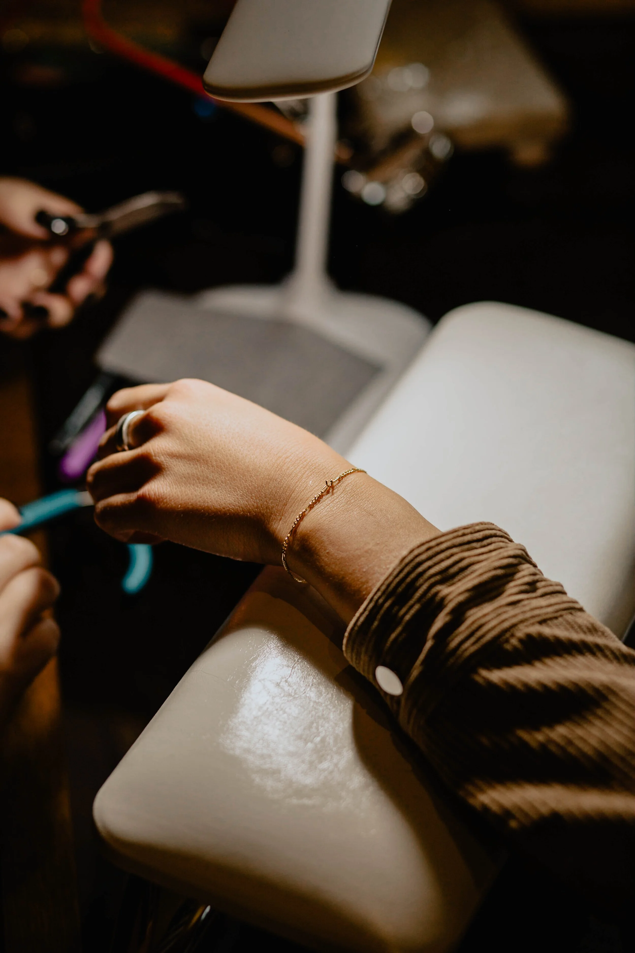 A person's hand with a gold bracelet and ring placing a piece of jewelry on a display stand during a jewelry crafting or selling process. Seattle professional head shot photography