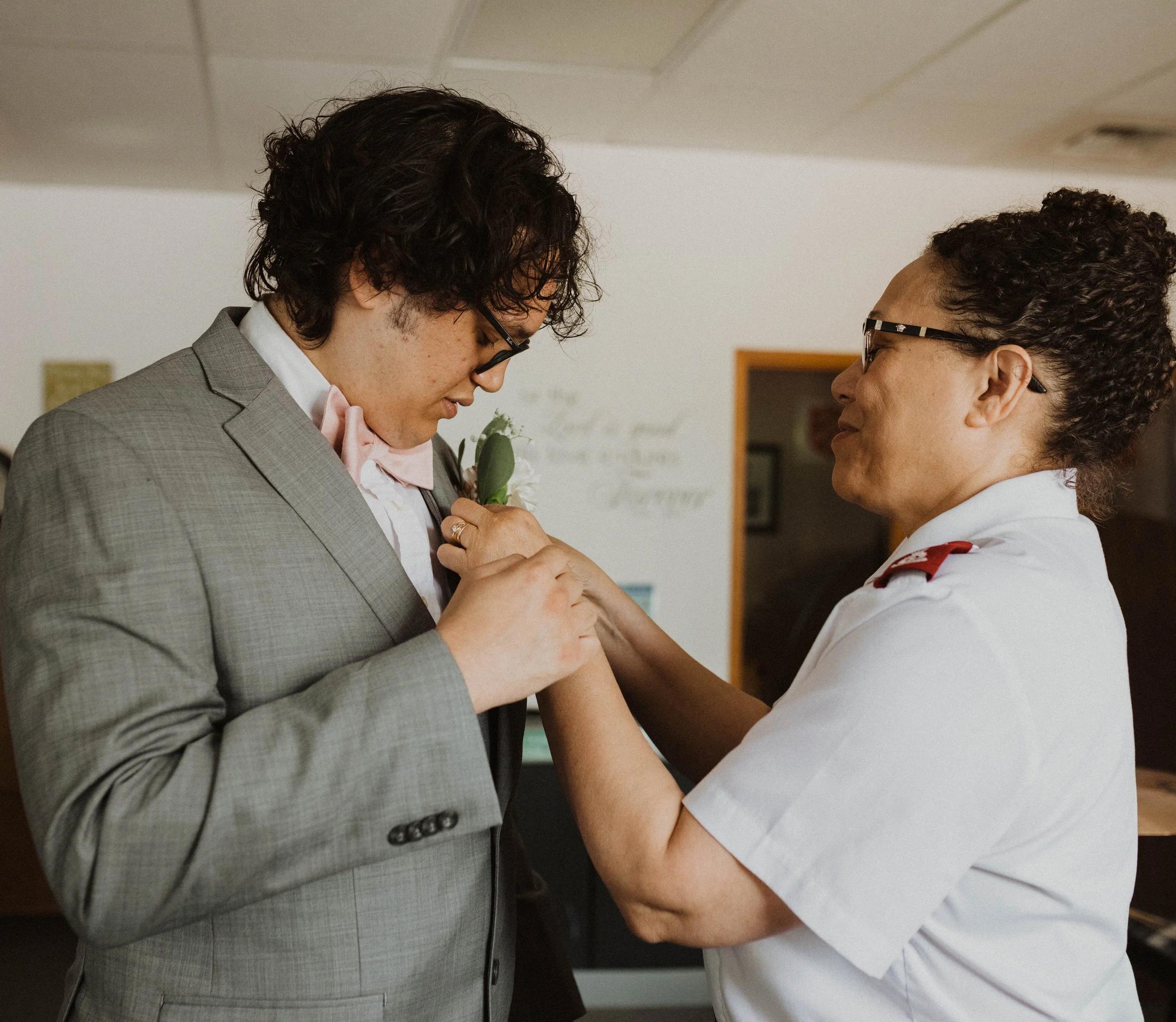 A man in a gray suit receiving a pin on his lapel from a woman in a white uniform, in an indoor setting. Seattle, WA wedding photography.
