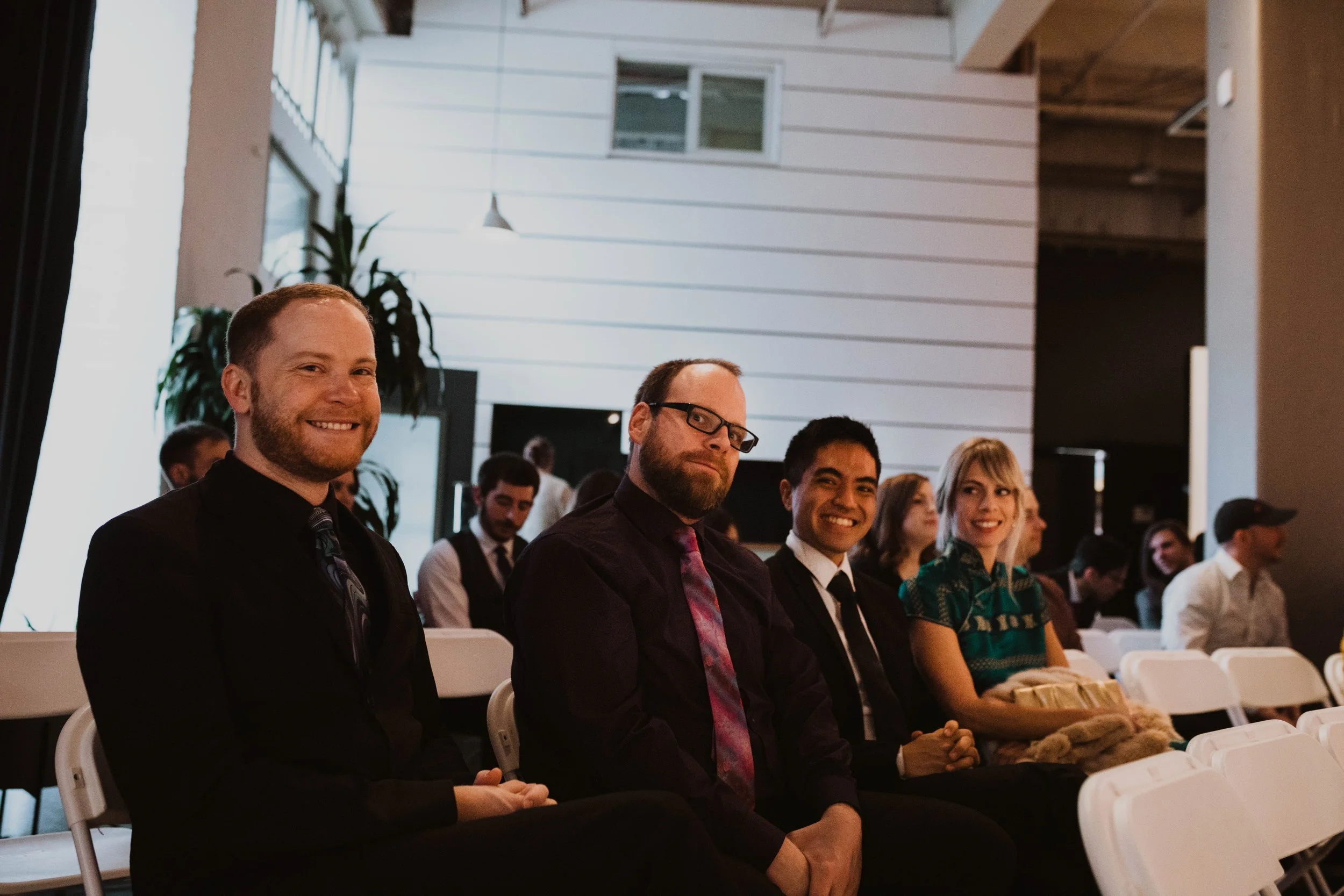 People sitting in chairs at a formal event, smiling and dressed in formal attire, with a modern interior background. Pioneer Square, Seattle, WA wedding photography.