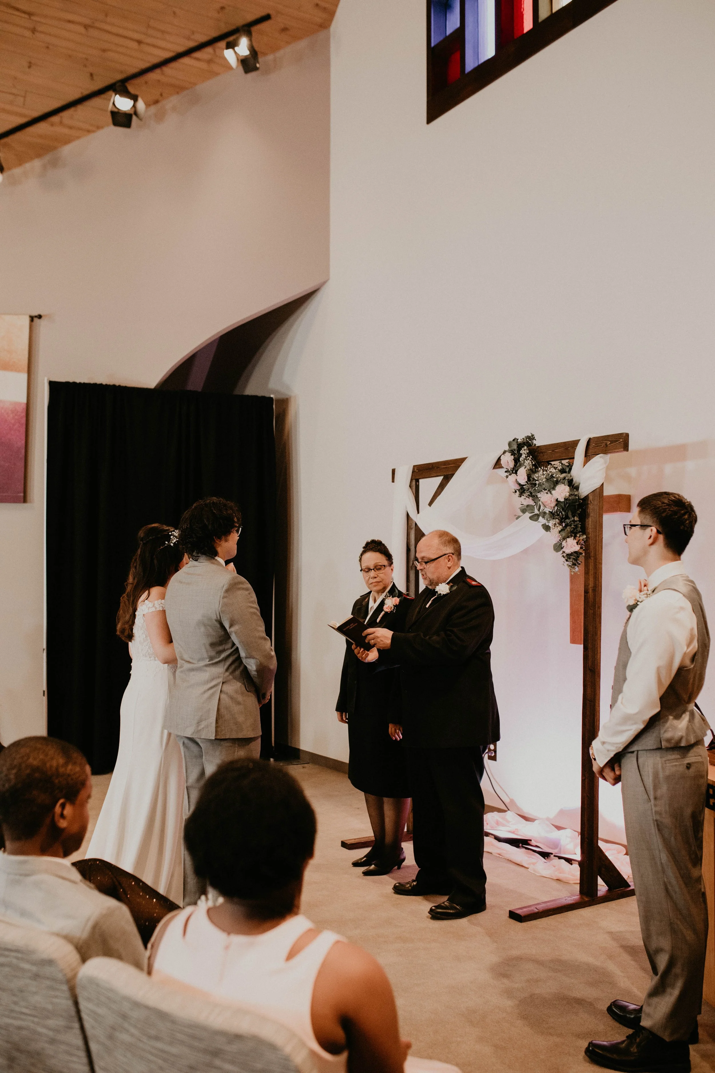 A wedding ceremony with a bride and groom standing before officiants, with guests seated watching, inside a church or wedding venue. Seattle, WA wedding photography.