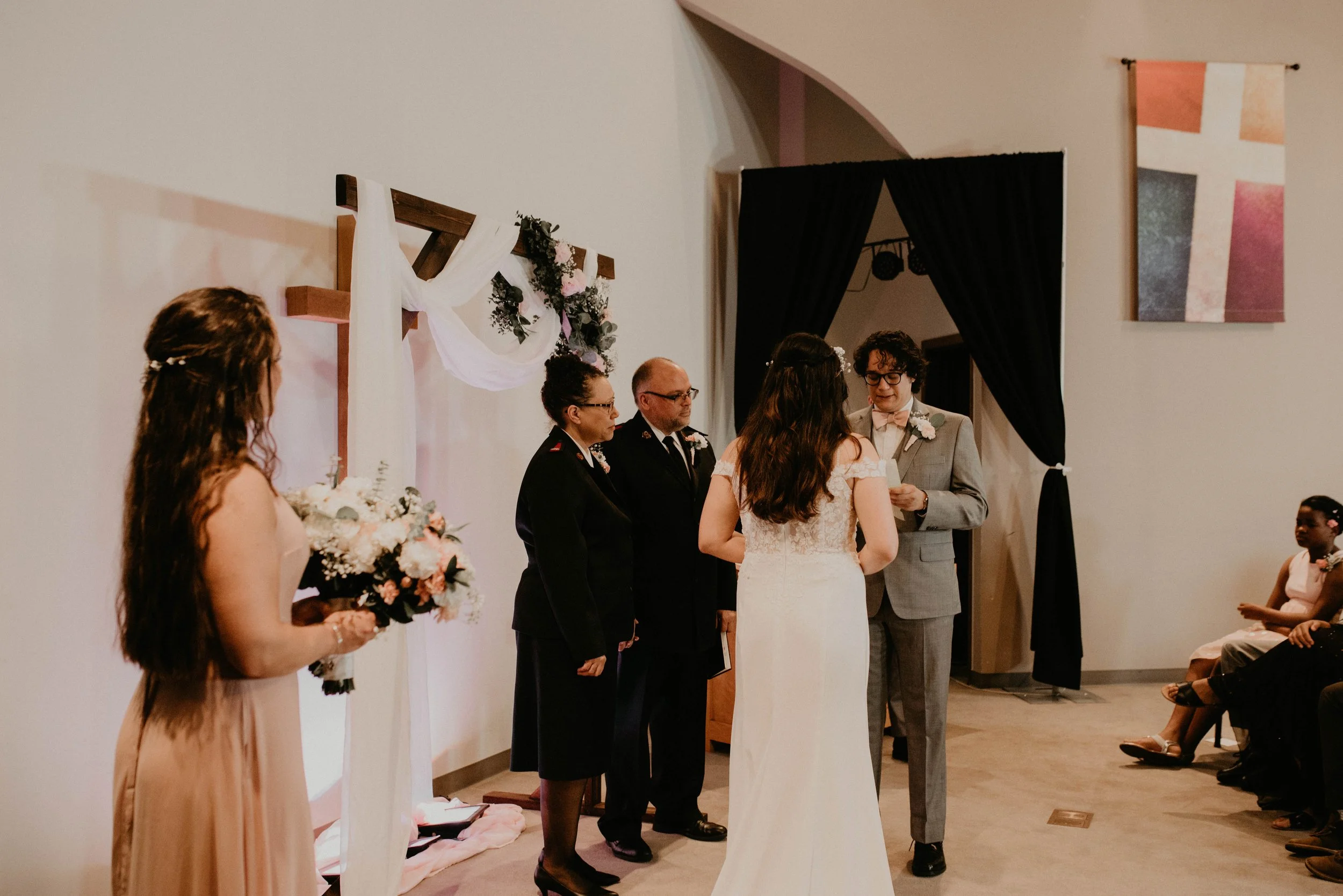 A wedding ceremony with a bride, groom, officiant, two witnesses, a maid of honor, and guests seated in a decorated indoor venue. Seattle, WA wedding photography.