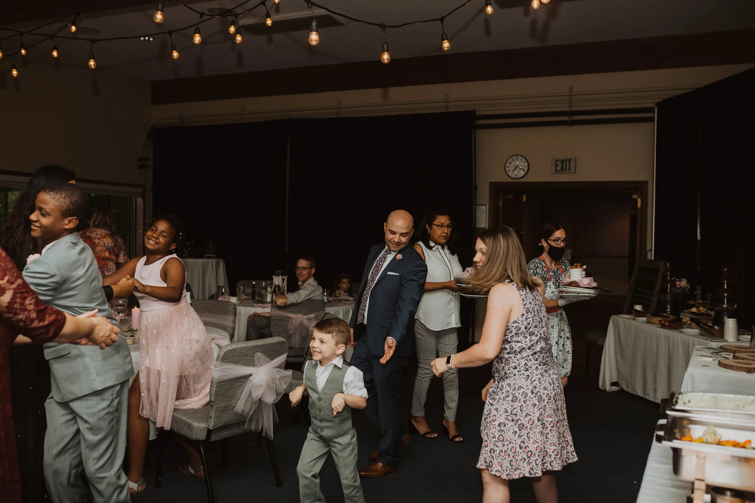People dancing and socializing at a celebration in a decorated indoor venue with string lights. Seattle, WA wedding photography.