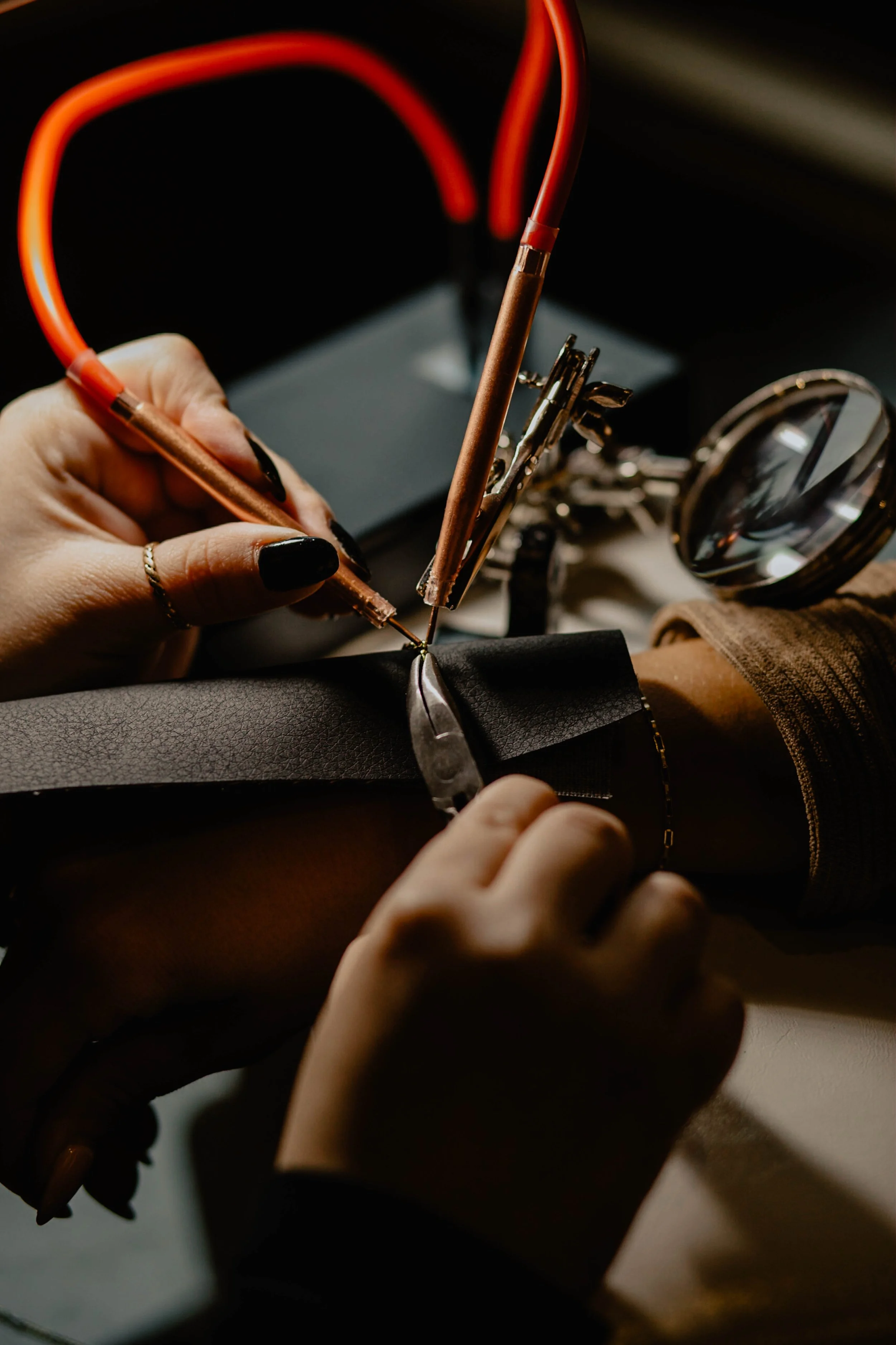 A person sewing black leather, holding a needle and thread, with tools and a magnifying glass nearby. Seattle professional head shot photography