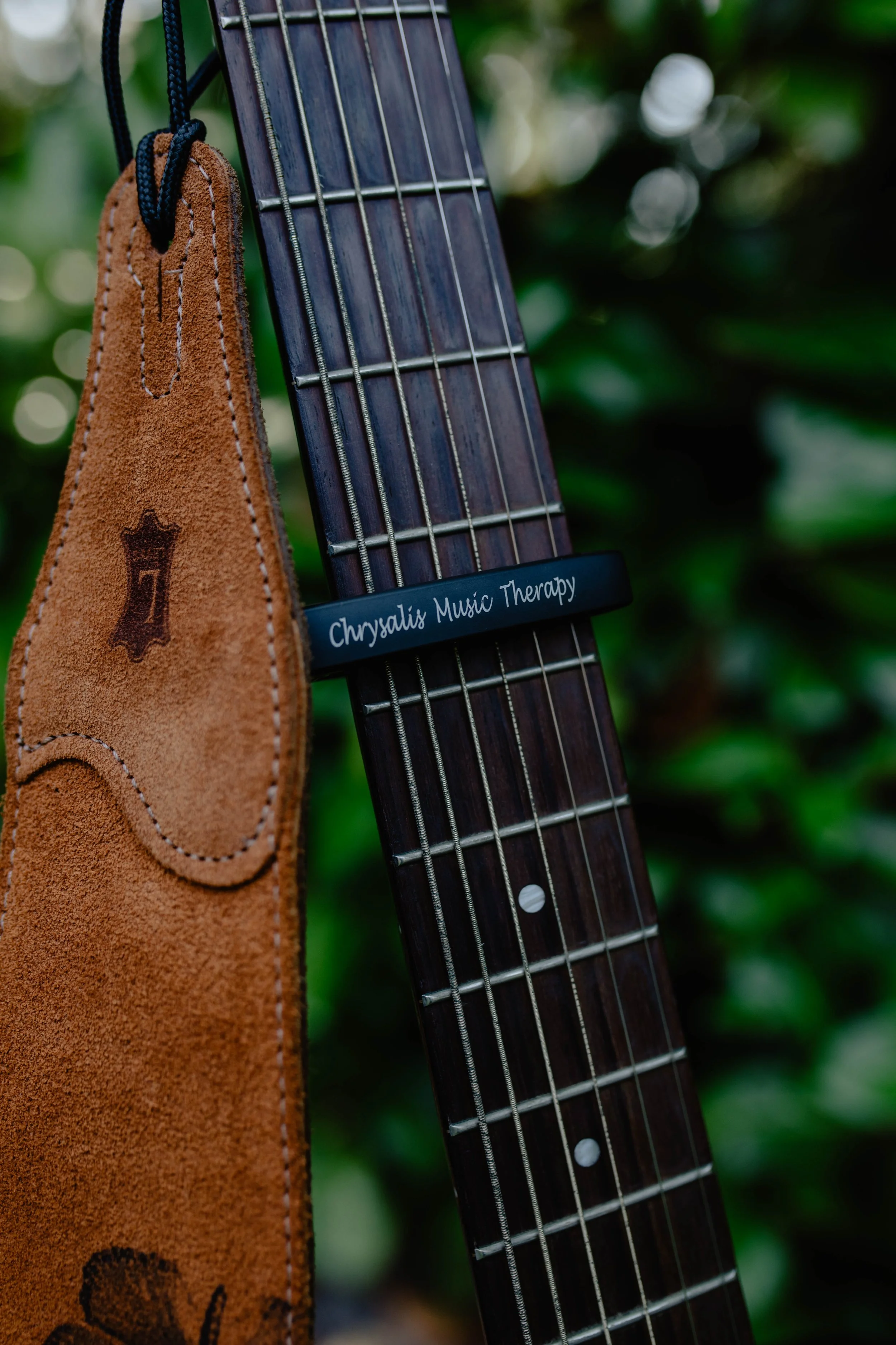 Guitar neck with a tag reading 'Chrysalis Music Therapy' and a leather strap hanging beside it. Seattle professional head shot photography