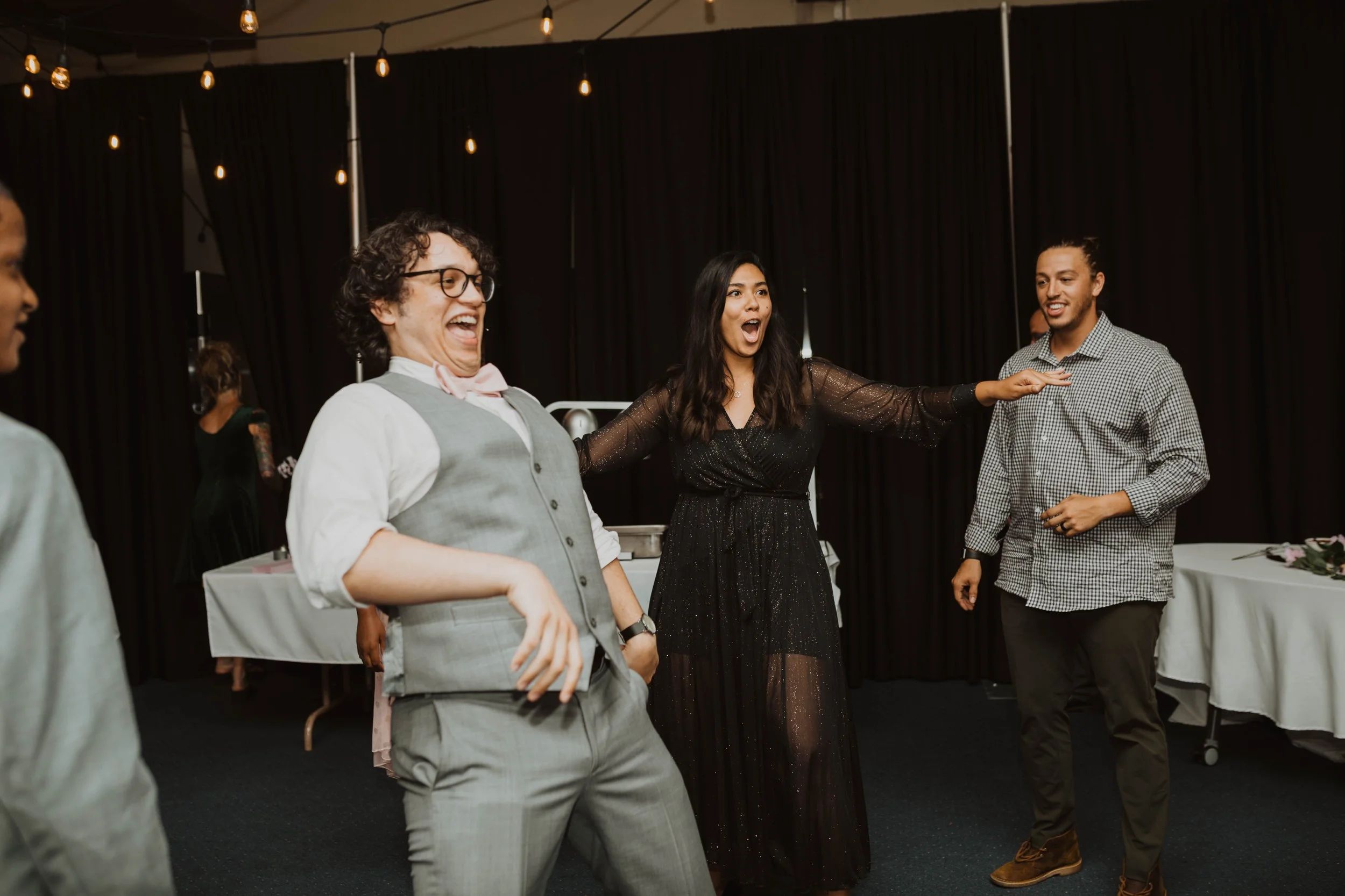 Group of people dancing and having fun at an indoor party or celebration, with warm lighting and decorated background. Seattle, WA wedding photography.