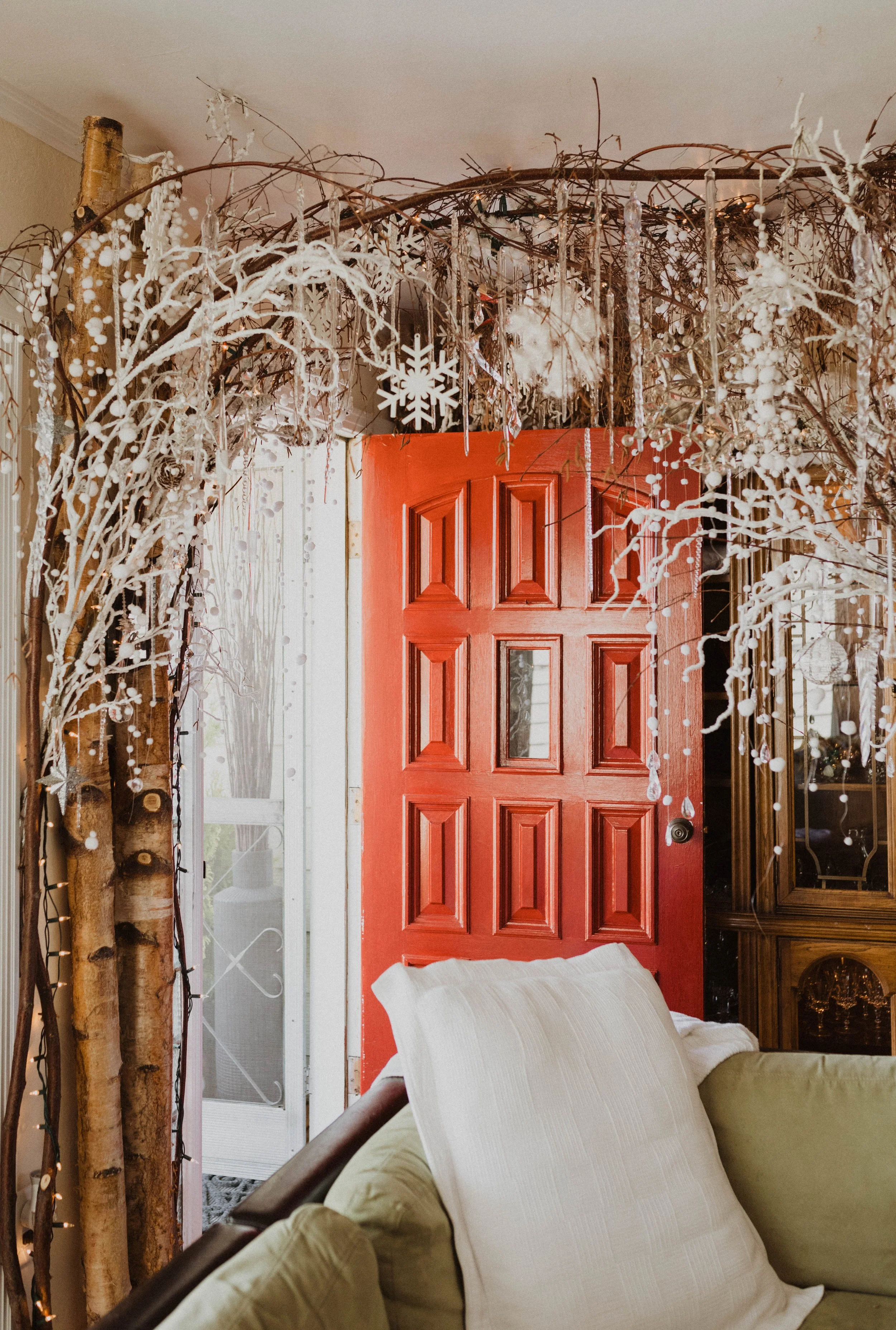 Decorated doorway with dried branches, white ornaments, and a red door in a cozy living room. Seattle, WA wedding photography.