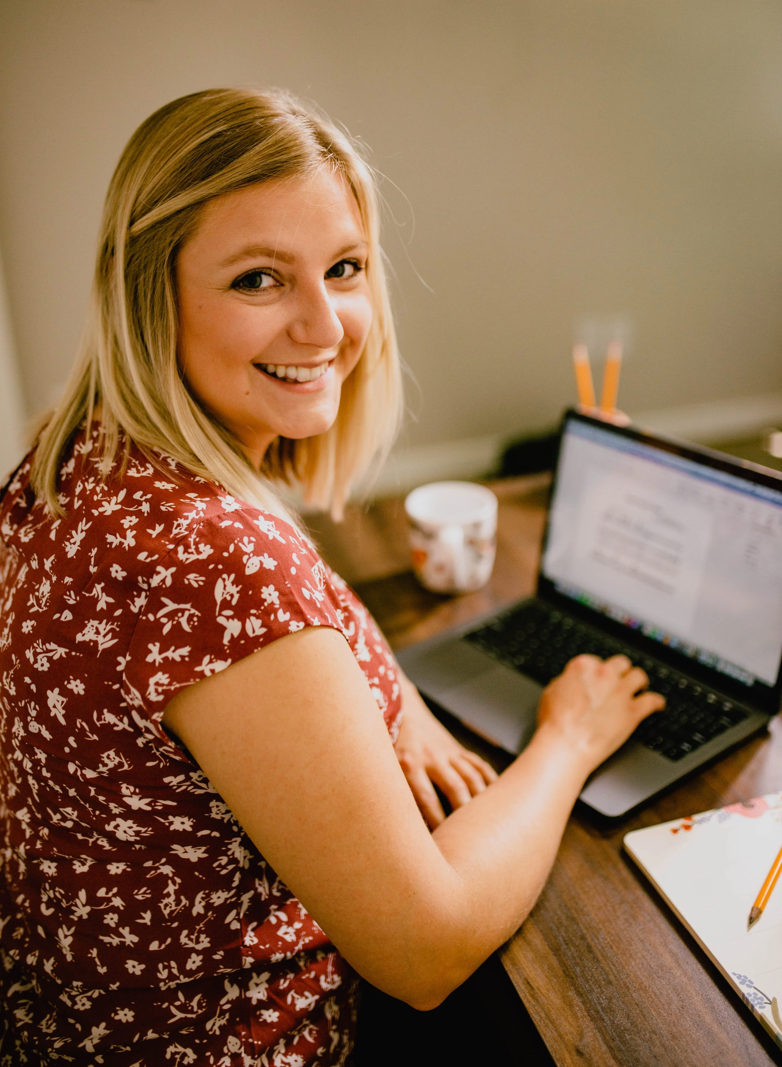 A woman with blonde hair smiling while working on a laptop at a desk. Seattle professional head shot photography