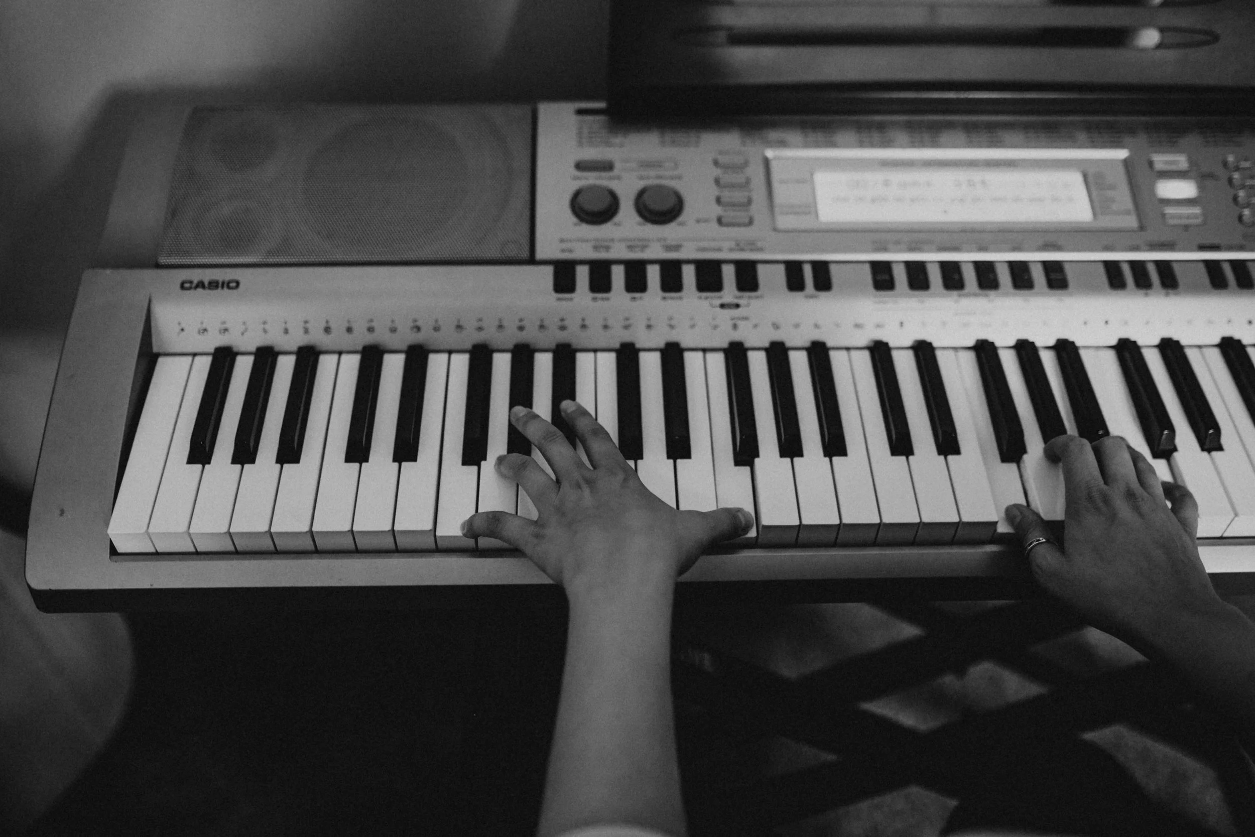Black and white photograph of a person playing a keyboard synthesizer with their hands, on a table with an audio mixer or keyboard. Seattle professional head shot photography