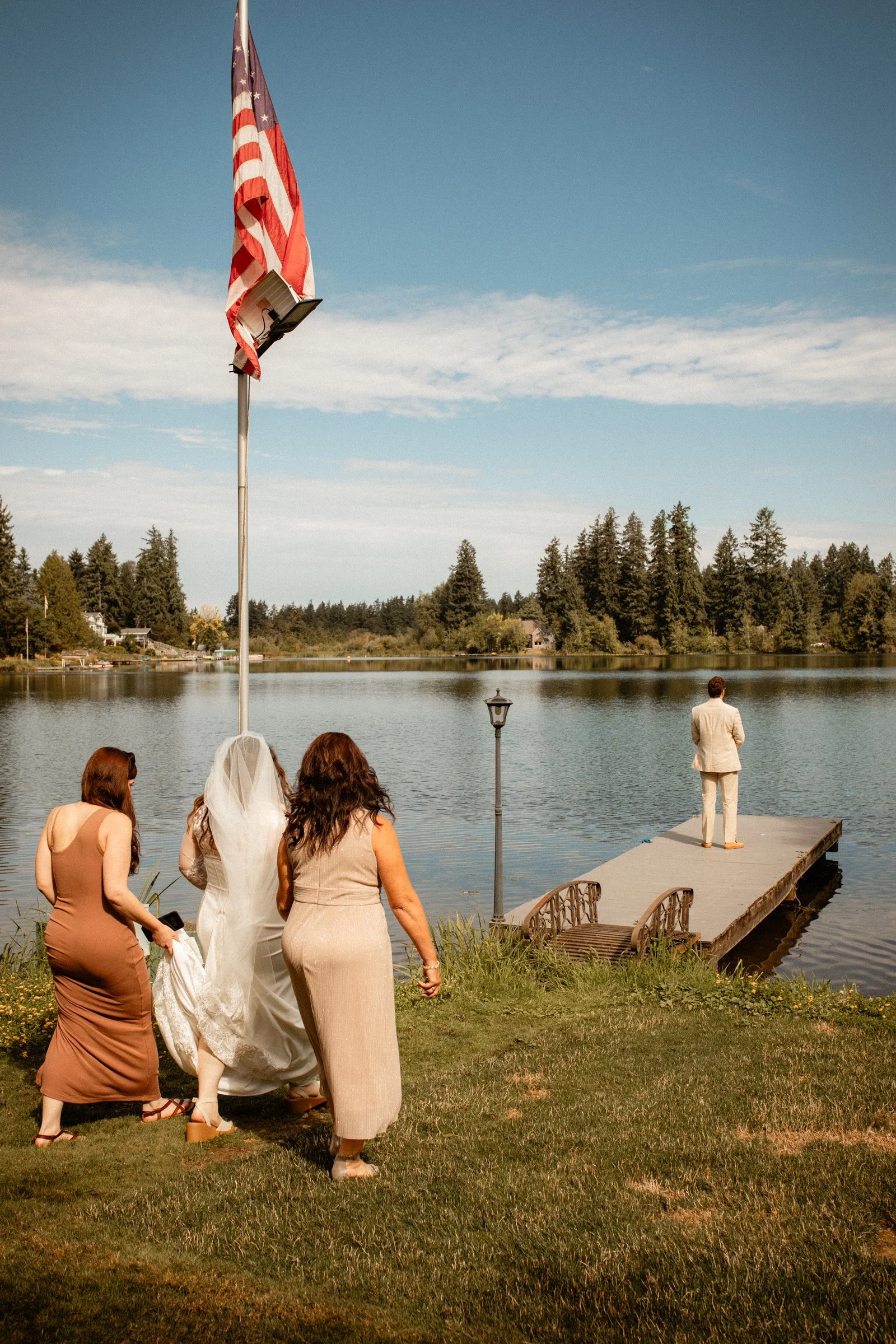 Maid of honor and mother of the bride escort the bride to her husband who's waiting on the dock of the lake for their wedding first look in Seattle, WA