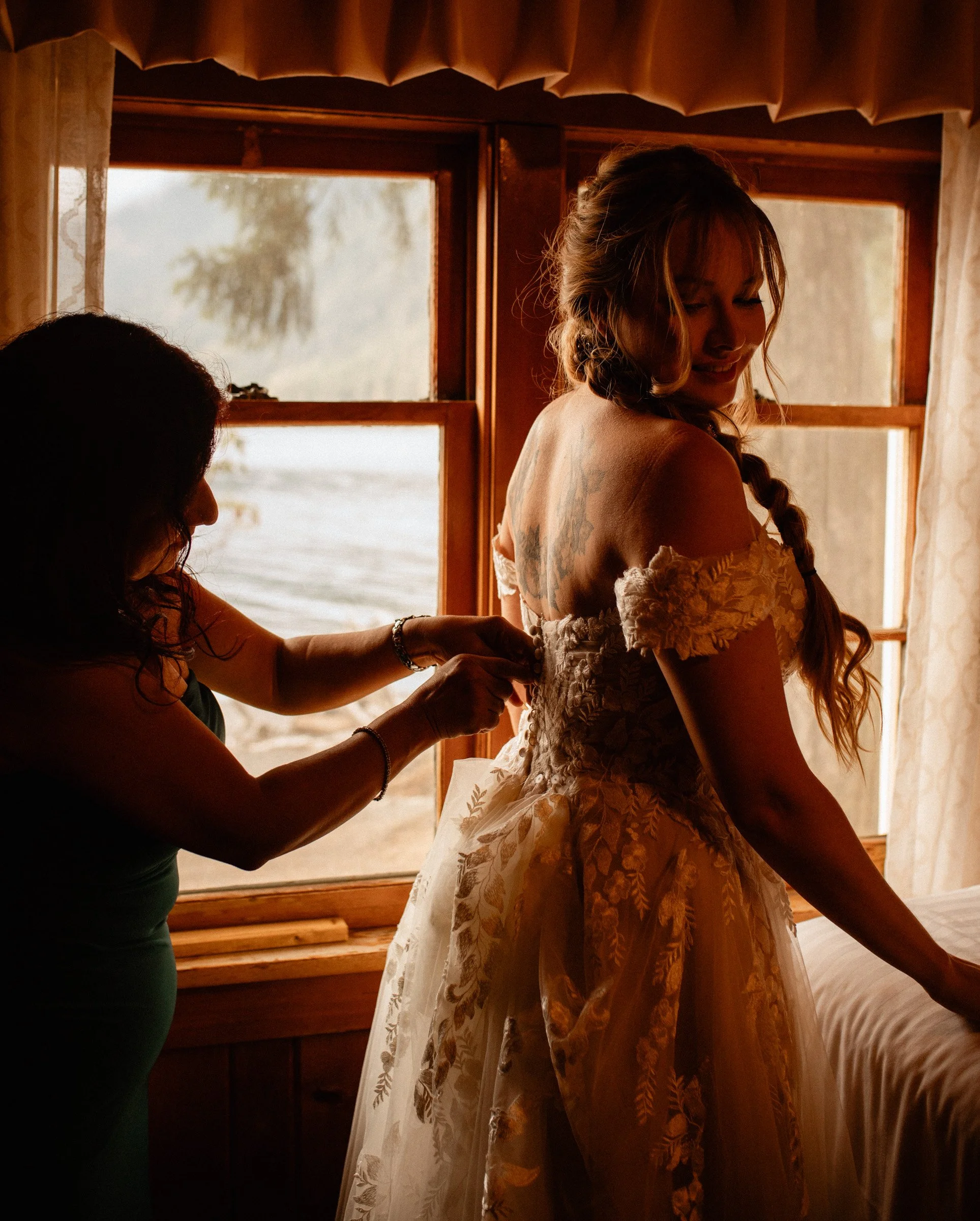 Mother of the bride helping her daughter into her dress inside the Lake Crescent Lodge bridal suite at Lake Crescent in Port Angeles, Washington.