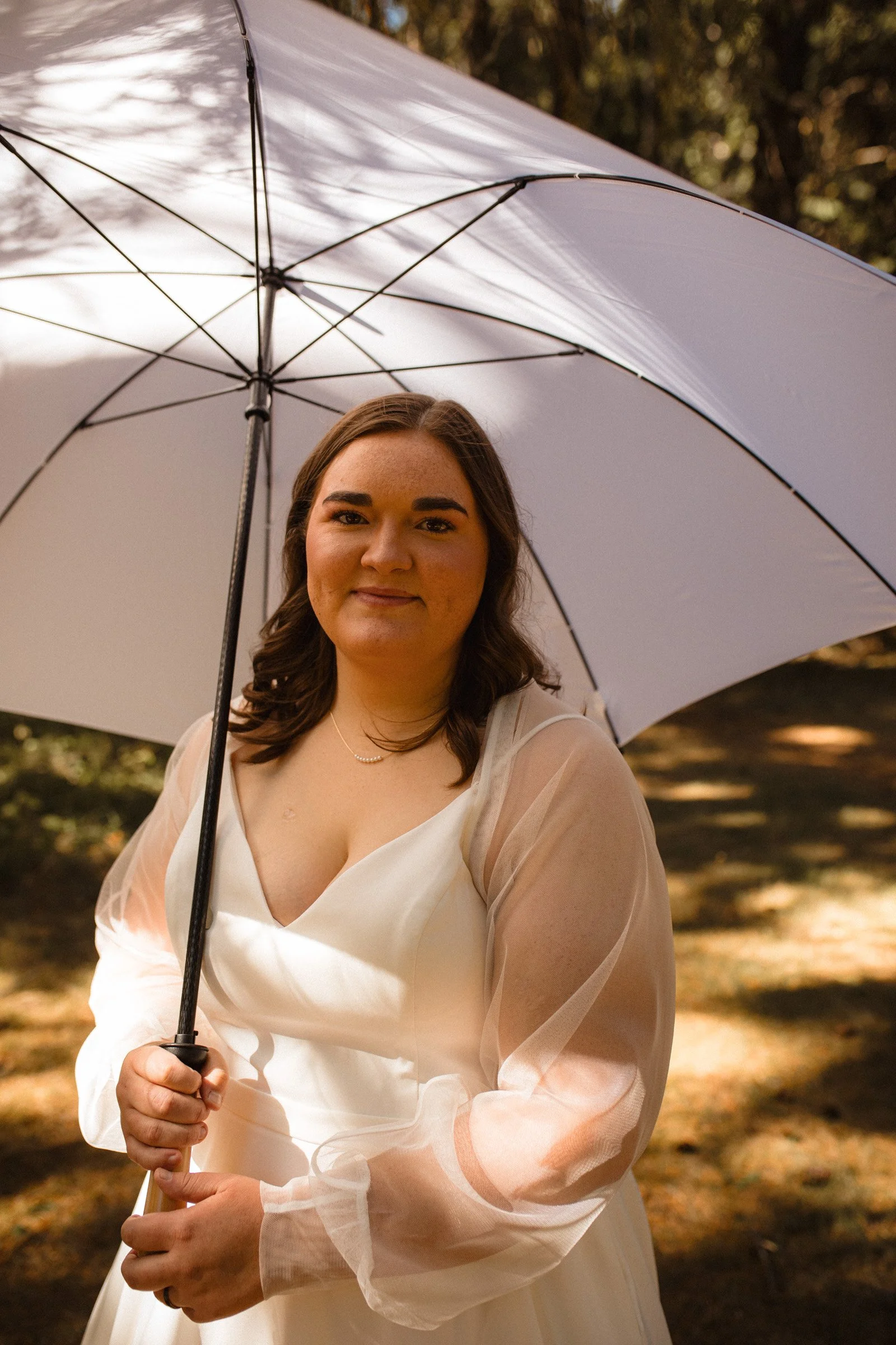 A bride stands in the forest shading herself with a white umbrella moments before she walks down the aisle of her wedding at Lake Crescent in Port Angeles, WA