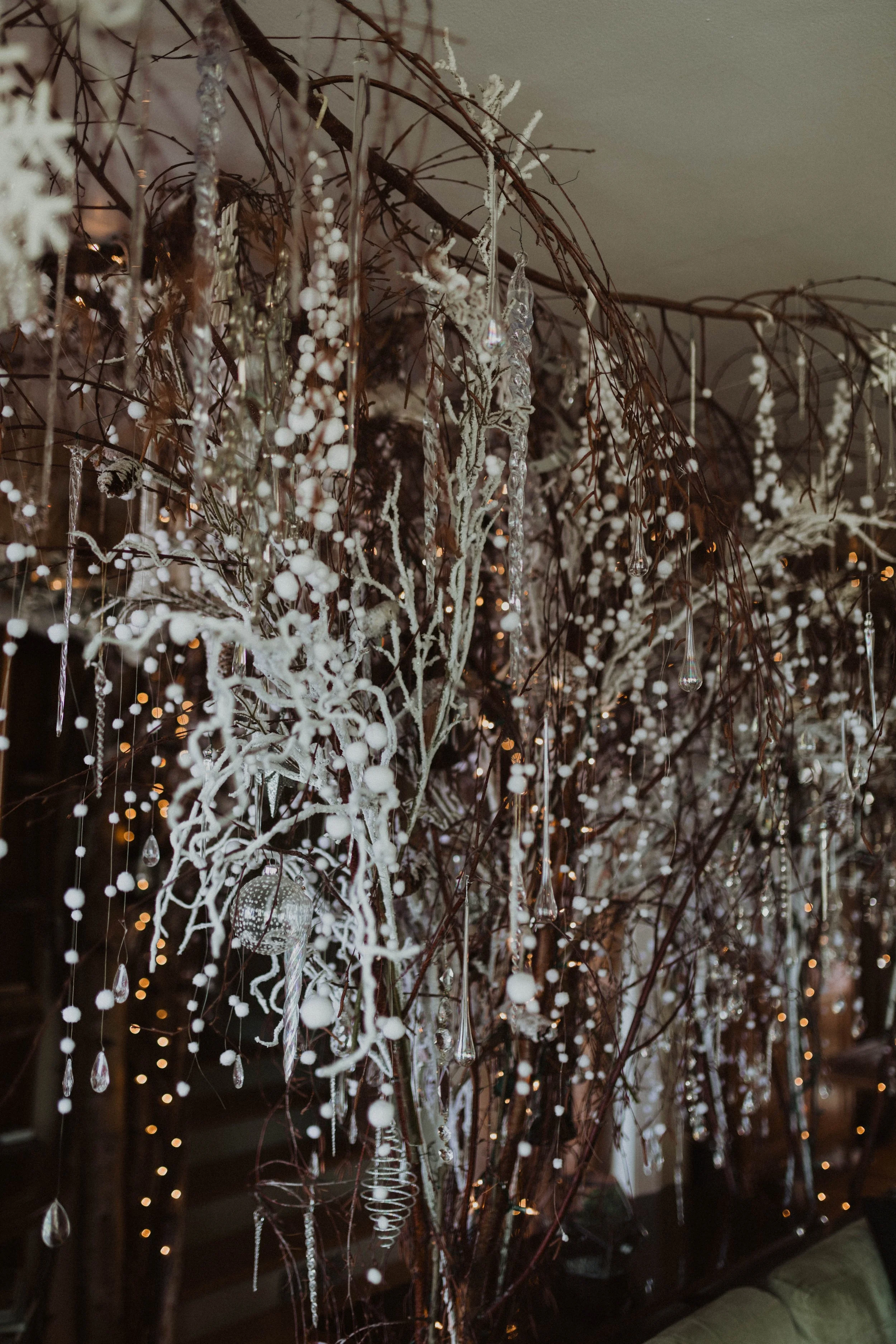 Decorative holiday branch with white ornaments, beads, and hanging crystals, illuminated by string lights. Seattle, WA wedding photography.