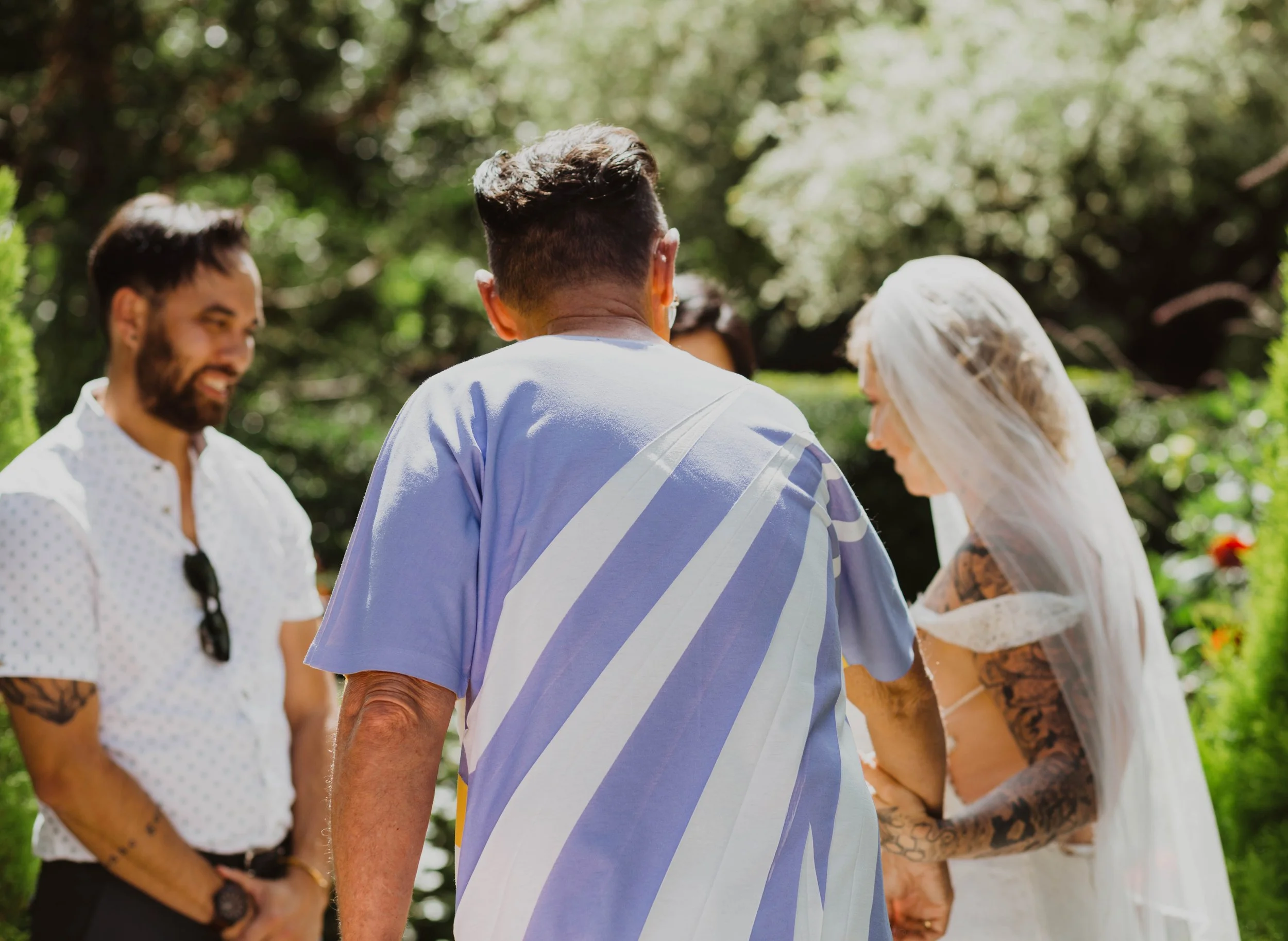 A wedding ceremony outdoor with a bride in a white dress and veil, an officiant, and a man in casual clothes, surrounded by greenery. Seattle, WA wedding photography.