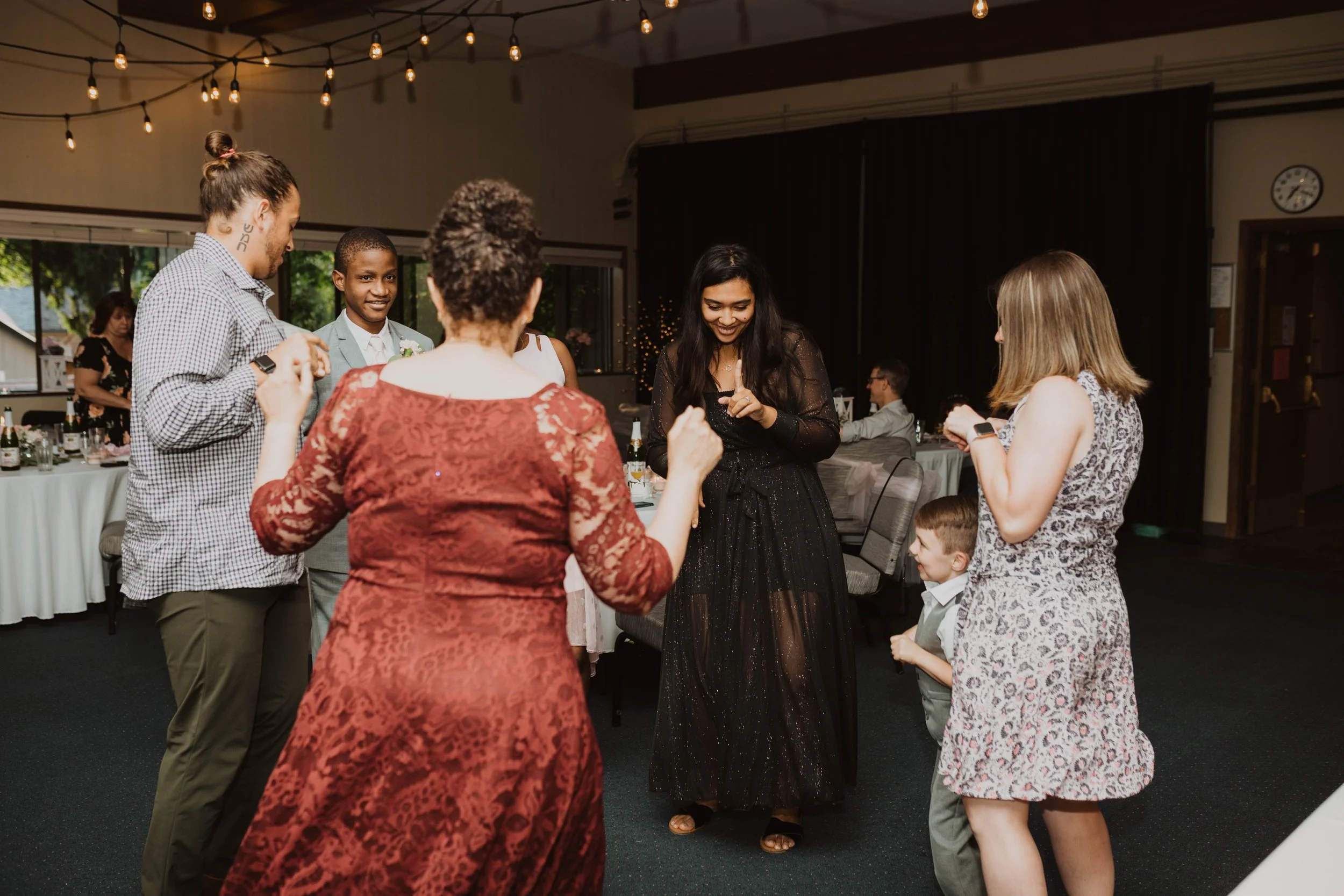 People dancing and having fun at a wedding reception in a decorated hall with string lights. Seattle, WA wedding photography.
