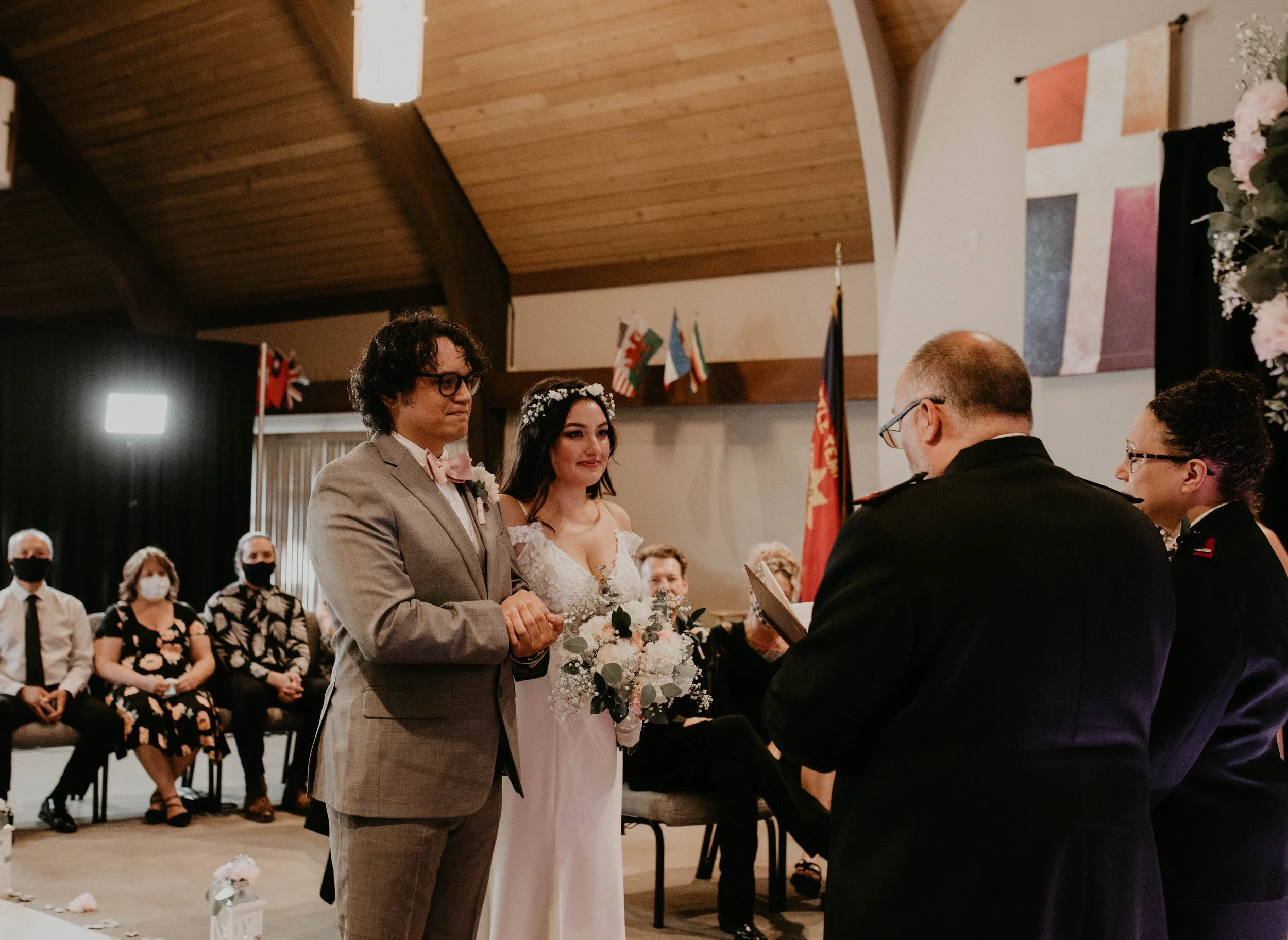 Wedding ceremony with bride and groom holding hands, officiant reading, guests seated, flags and artwork in background. Seattle, WA wedding photography.