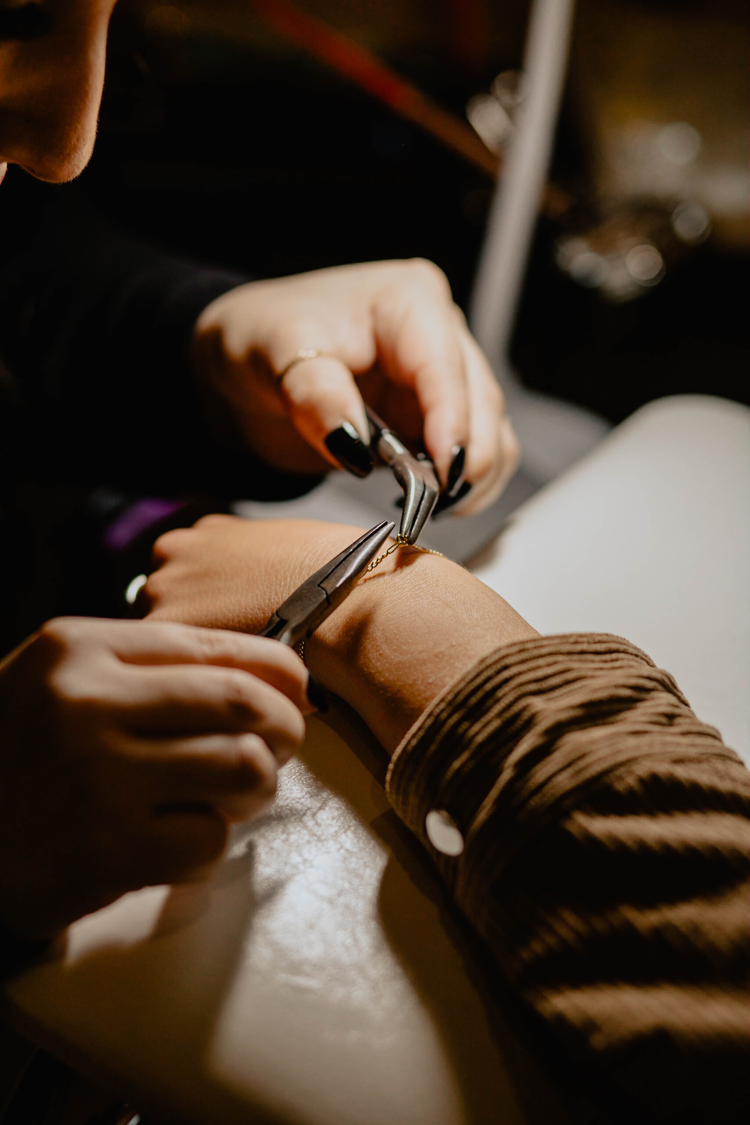 A jewelry artist is attaching a gold chain to a bracelet on a client's wrist using pliers and tweezers. Seattle professional head shot photography