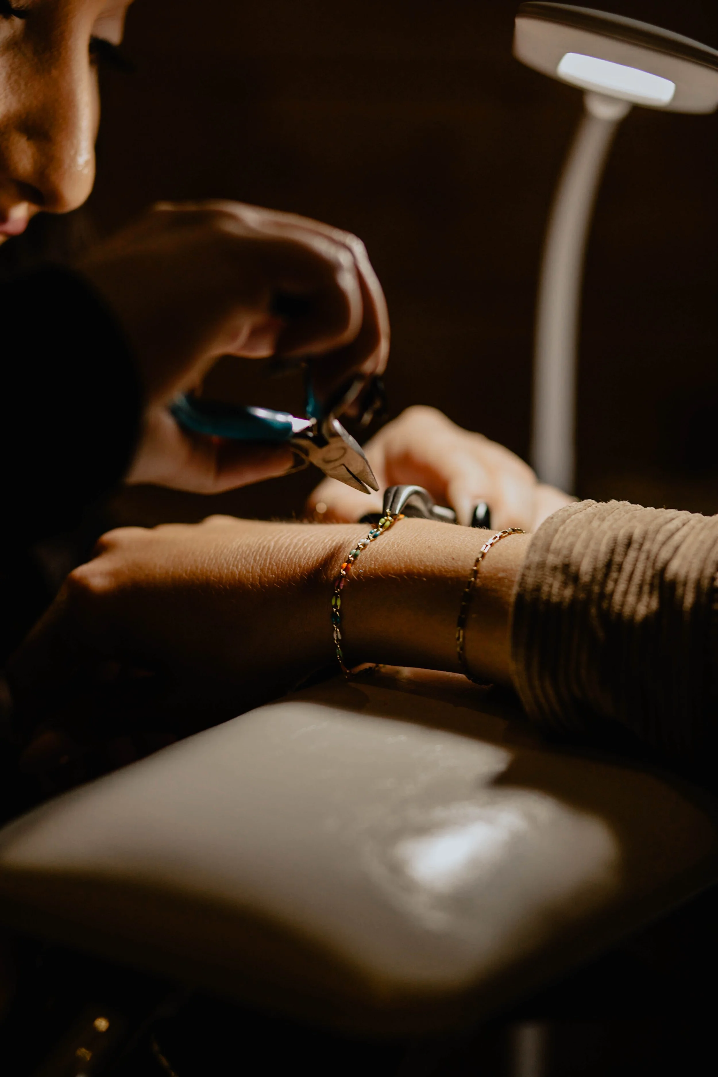 A person getting a tattoo with a tattoo artist using a tattoo machine under a lamp, on their wrist adorned with multiple bracelets. Seattle professional head shot photography