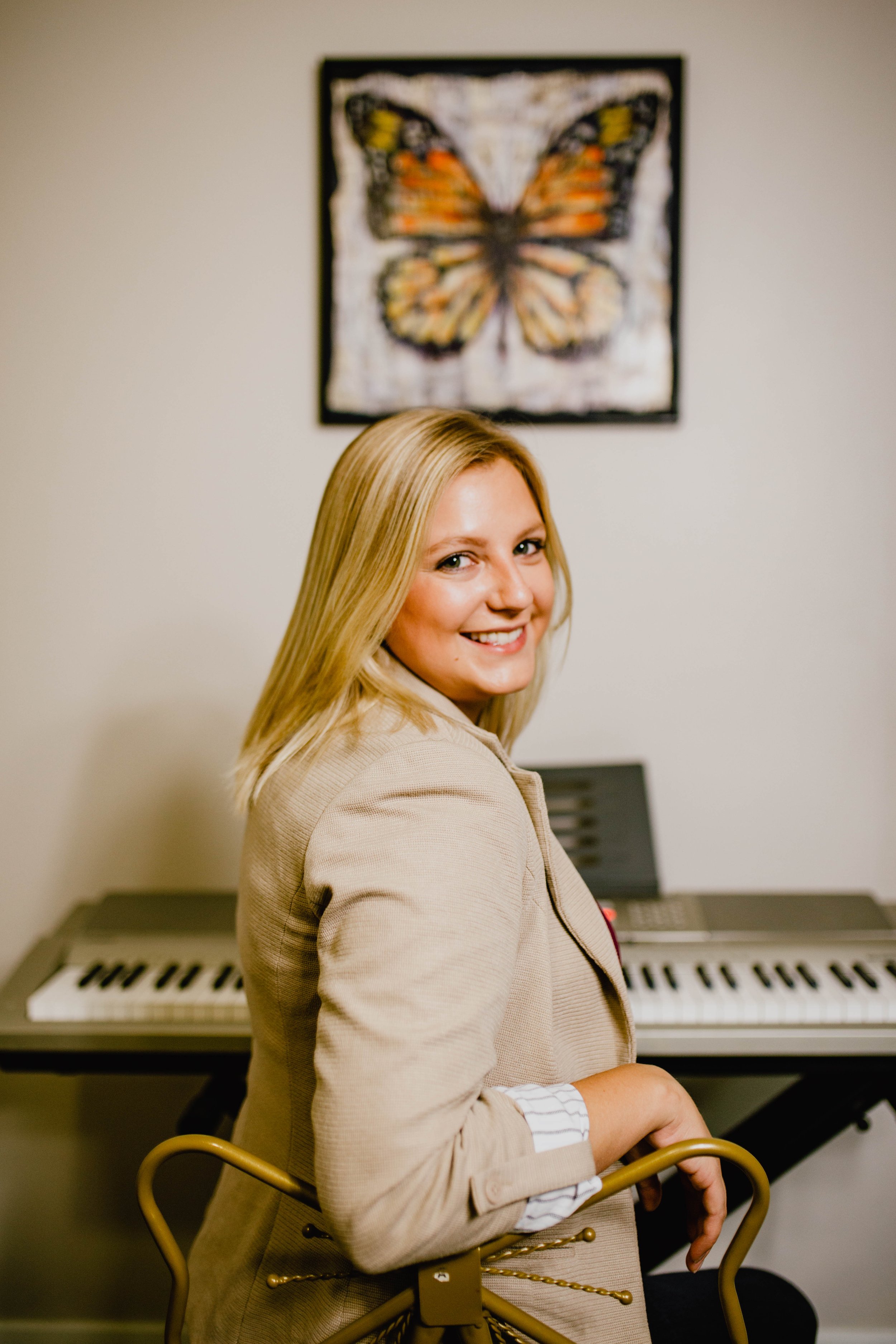 A woman with blonde hair smiling at the camera, sitting in front of a keyboard and a butterfly picture on the wall behind her. Seattle professional head shot photography