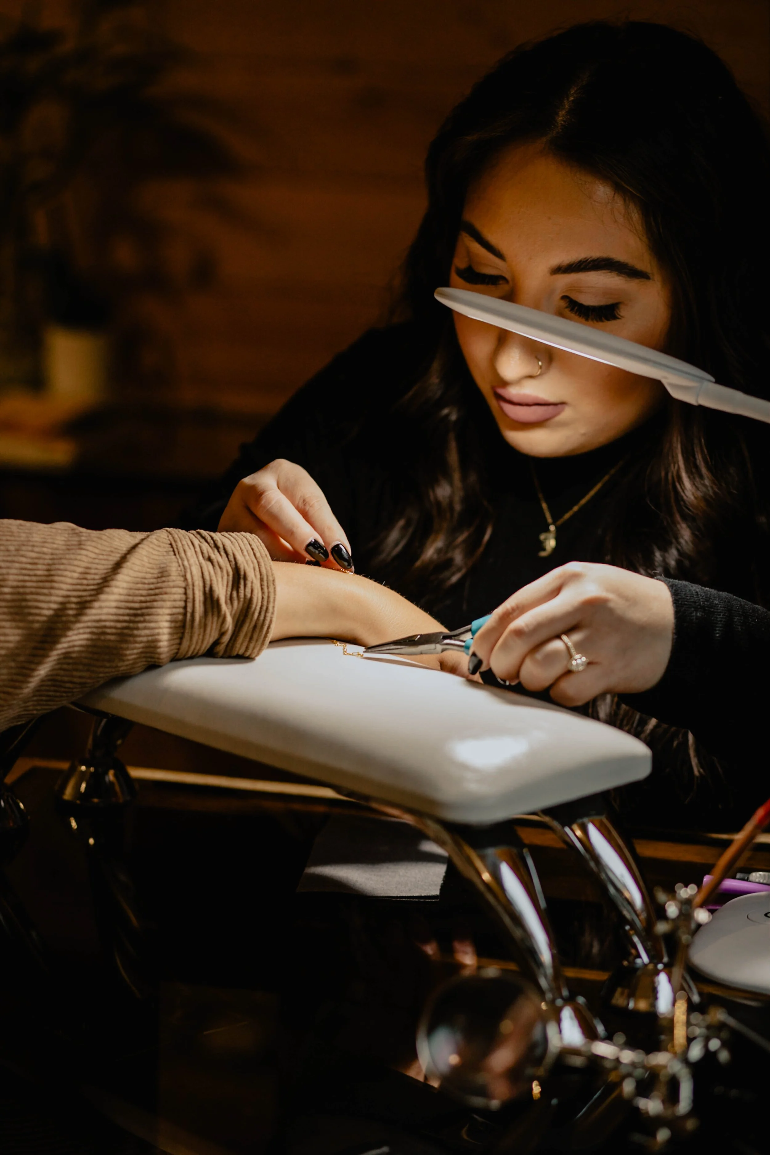 A woman with dark hair and a nose piercing gets a tattoo on her forearm from a tattoo artist in a tattoo studio. Seattle professional head shot photography