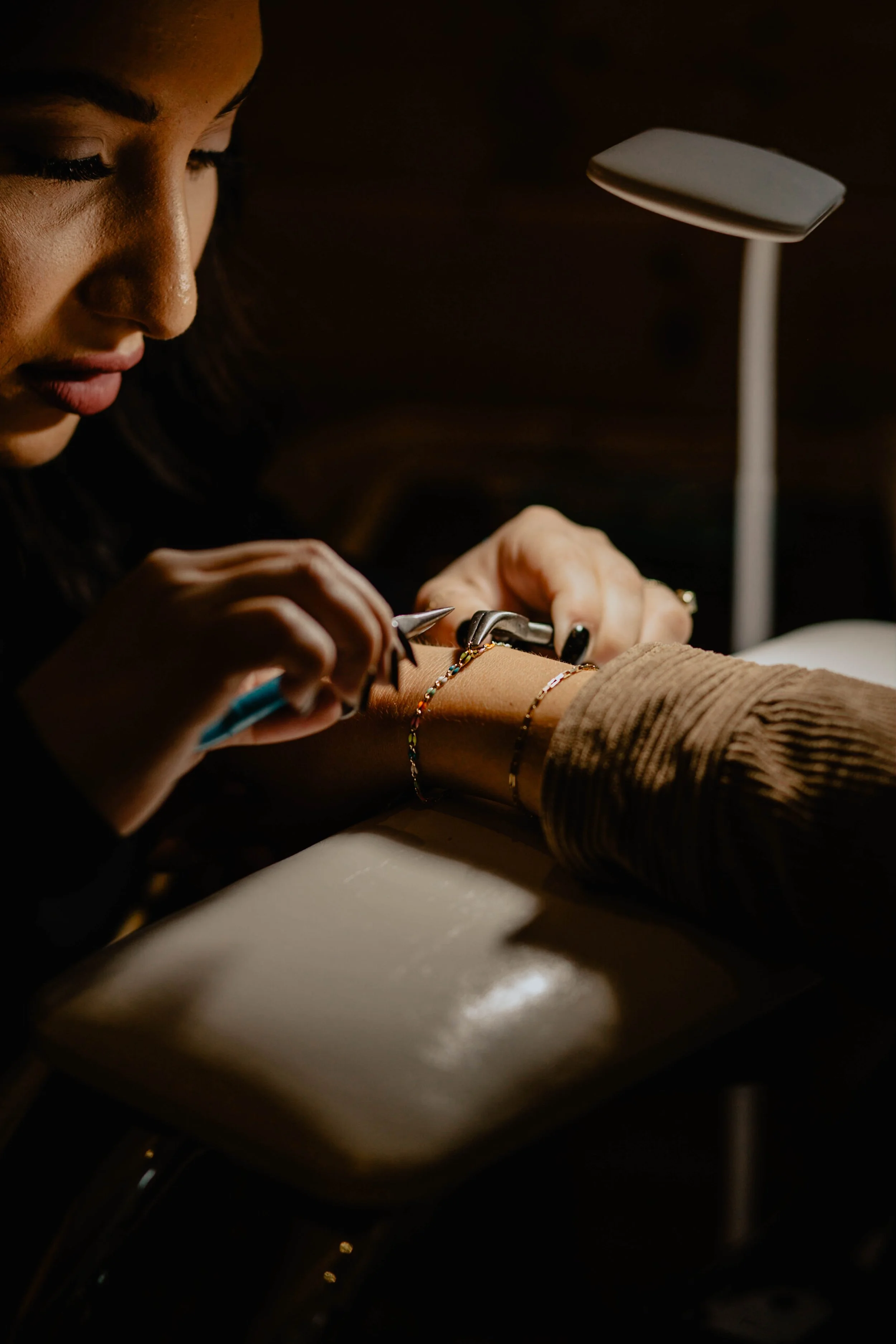 A woman getting a manicure, applying nail polish to a client's nails in a dimly lit setting. Seattle professional head shot photography