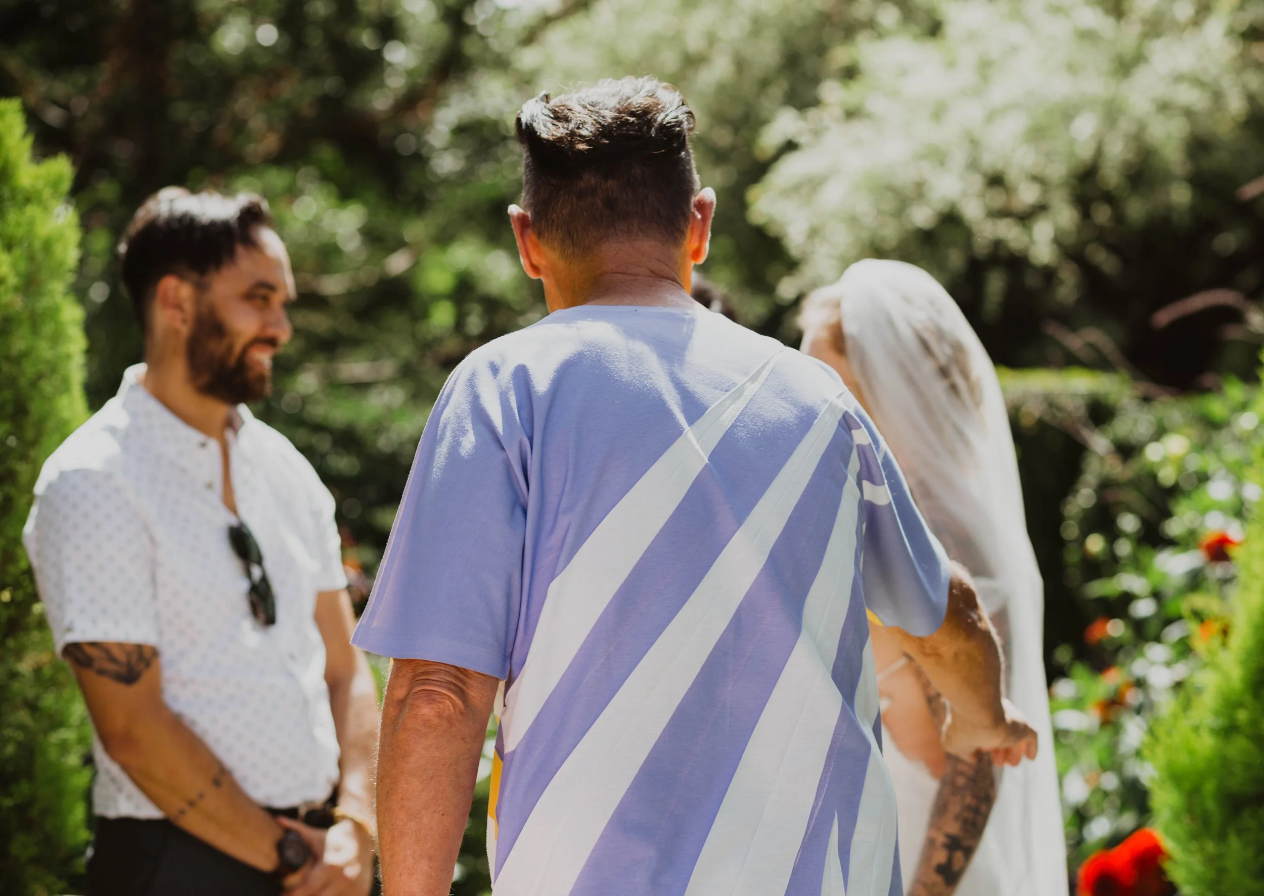 People standing outdoors in a garden during daytime, with sunlight filtering through trees. Seattle, WA wedding photography.