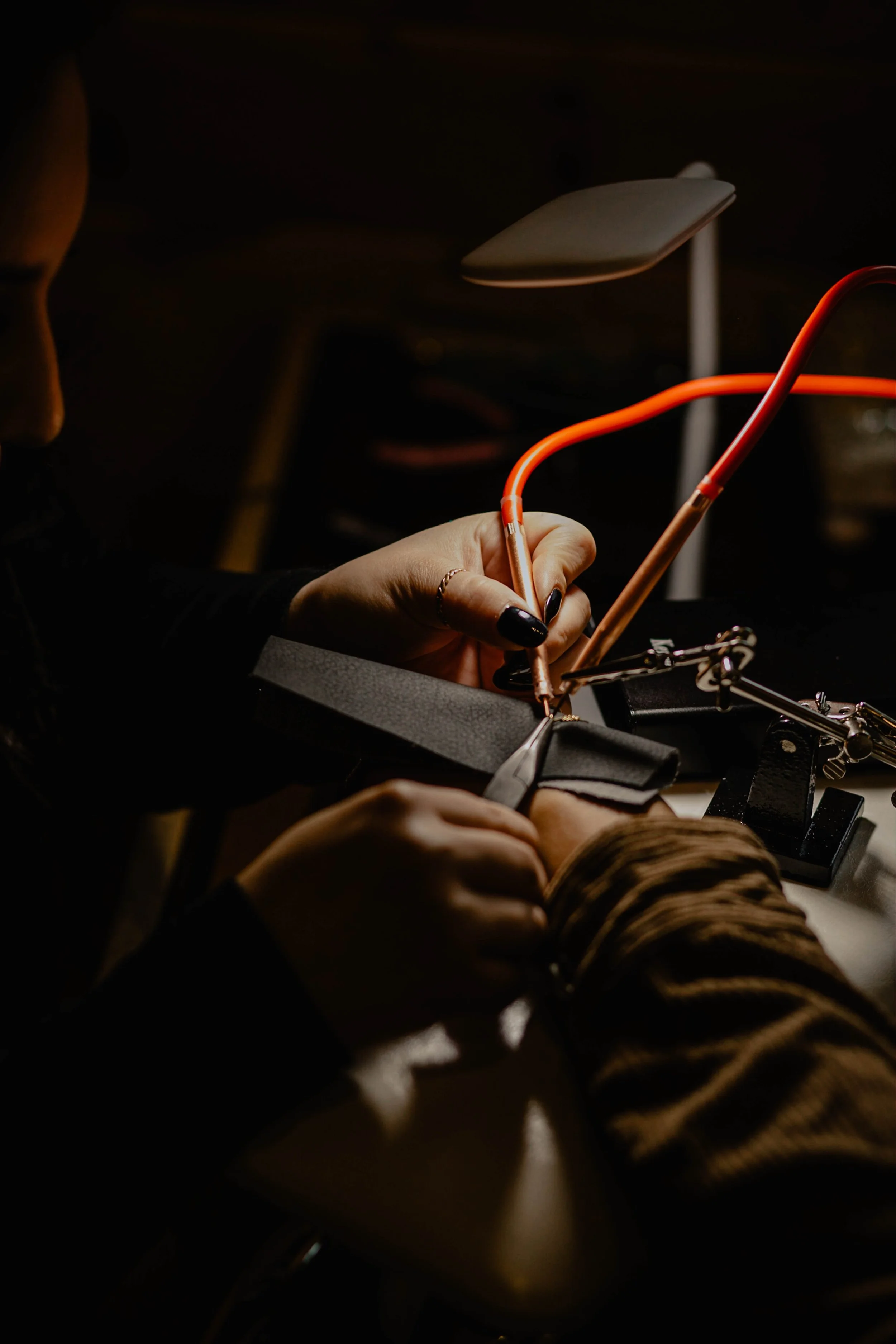 A person is soldering a piece of leather or fabric at a workbench with a soldering iron and tools, with a focused task in a dimly lit environment. Seattle professional head shot photography