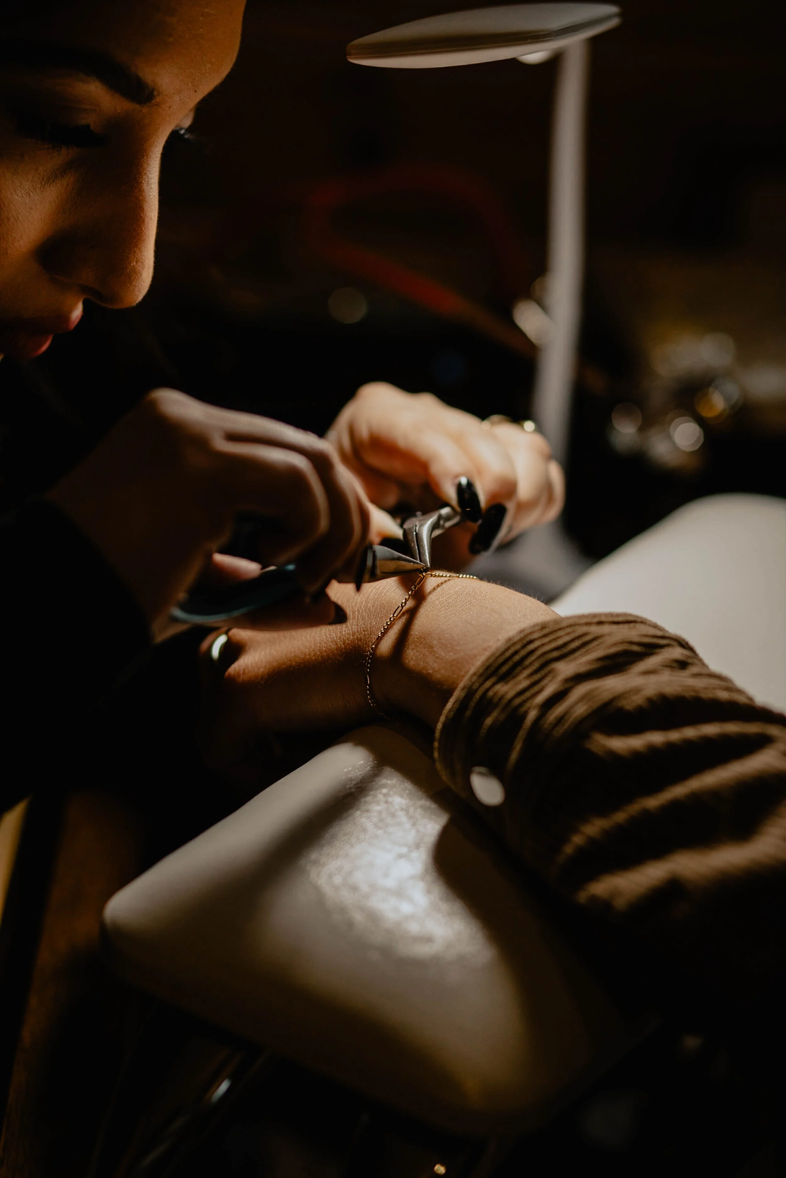 A woman is jewelry making, working on a gold necklace with a jewelry tool in a dimly lit room. Seattle professional head shot photography