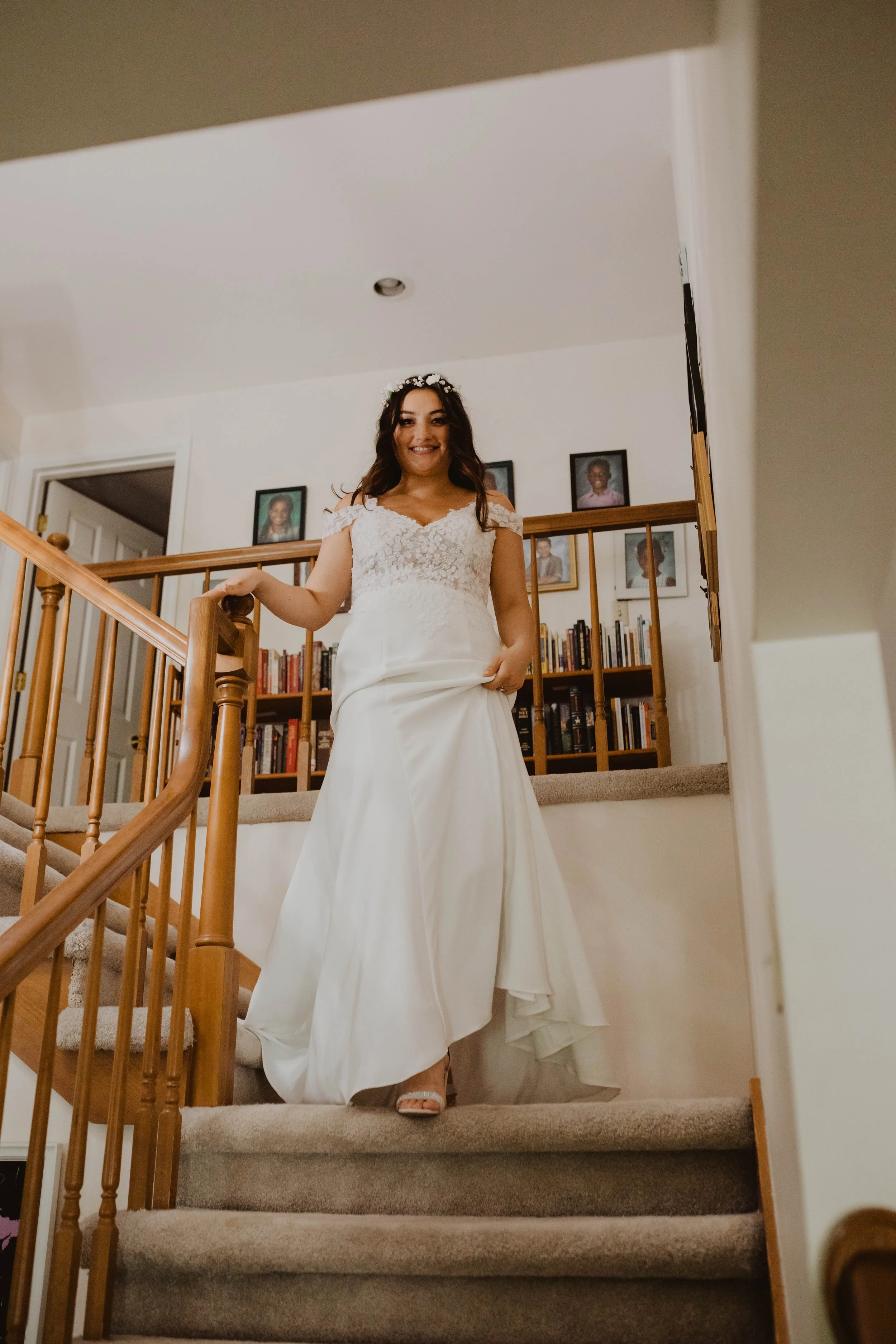 A woman in a white wedding dress and floral headband standing on staircase, holding the railing and smiling. Seattle, WA wedding photography.