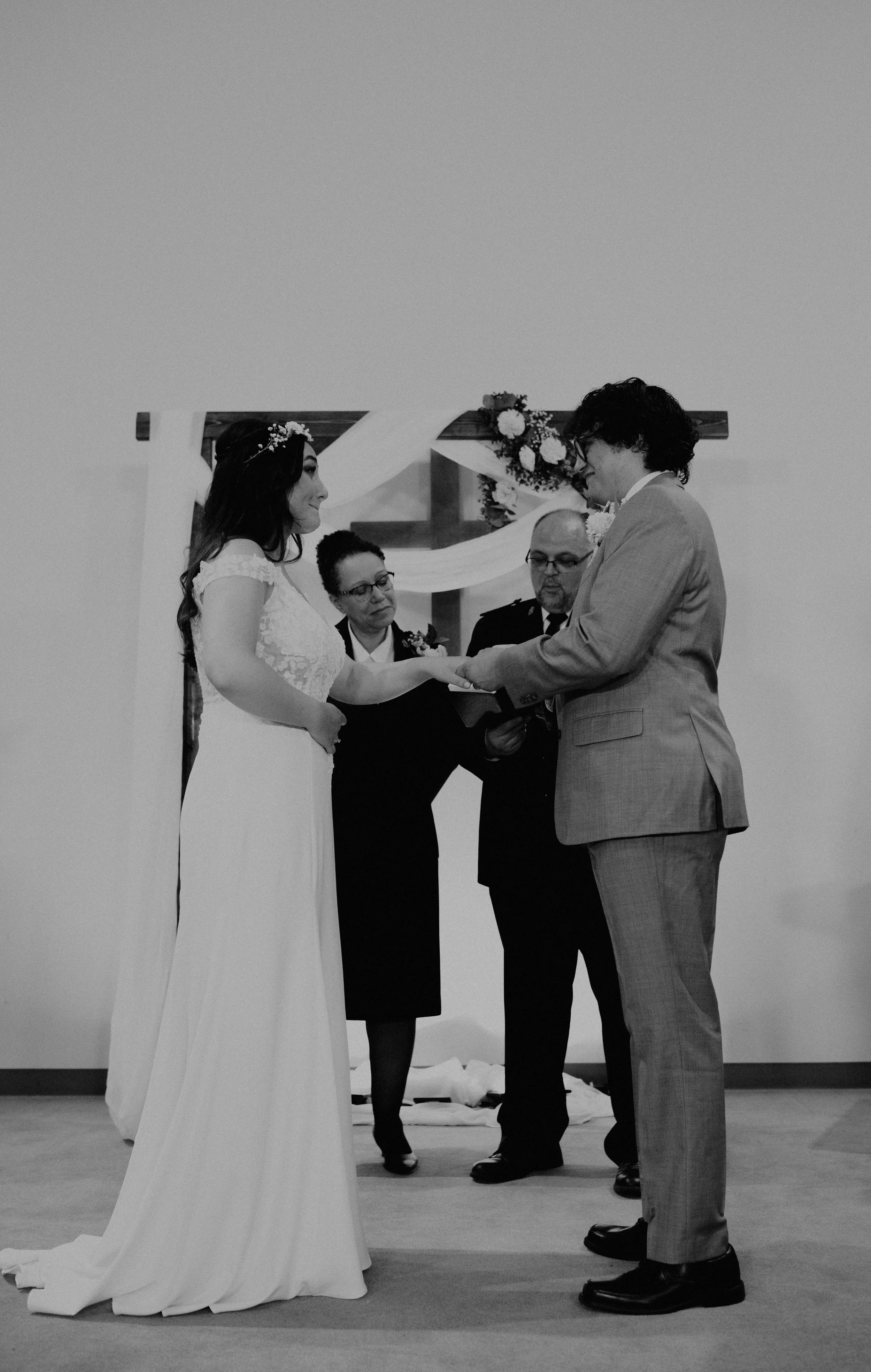 A couple getting married, holding hands during the ceremony, with two officiants in the background and a decorative floral backdrop. Seattle, WA wedding photography.